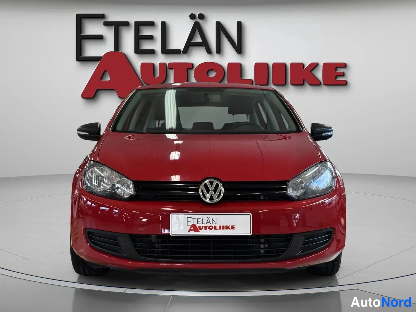 Edestä: Punaisen Volkswagen Golfin etunäkymä, grilli ja etupyran valot showroomissa.