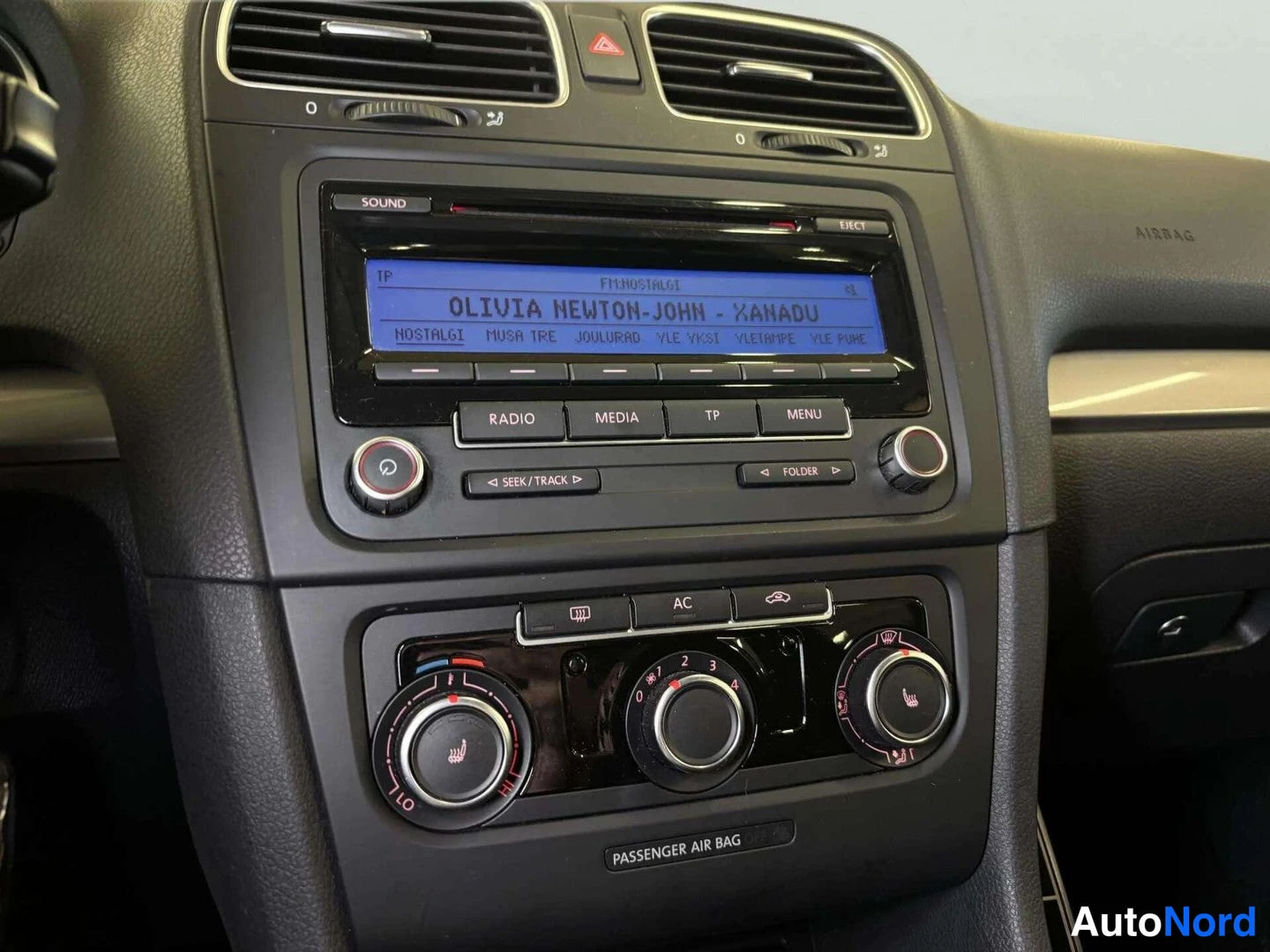 Etuviisto: Kojelauta: radio- ja media-yksikkö, ilmastointi (AC) -painike ja PASSENGER AIR BAG -merkintä