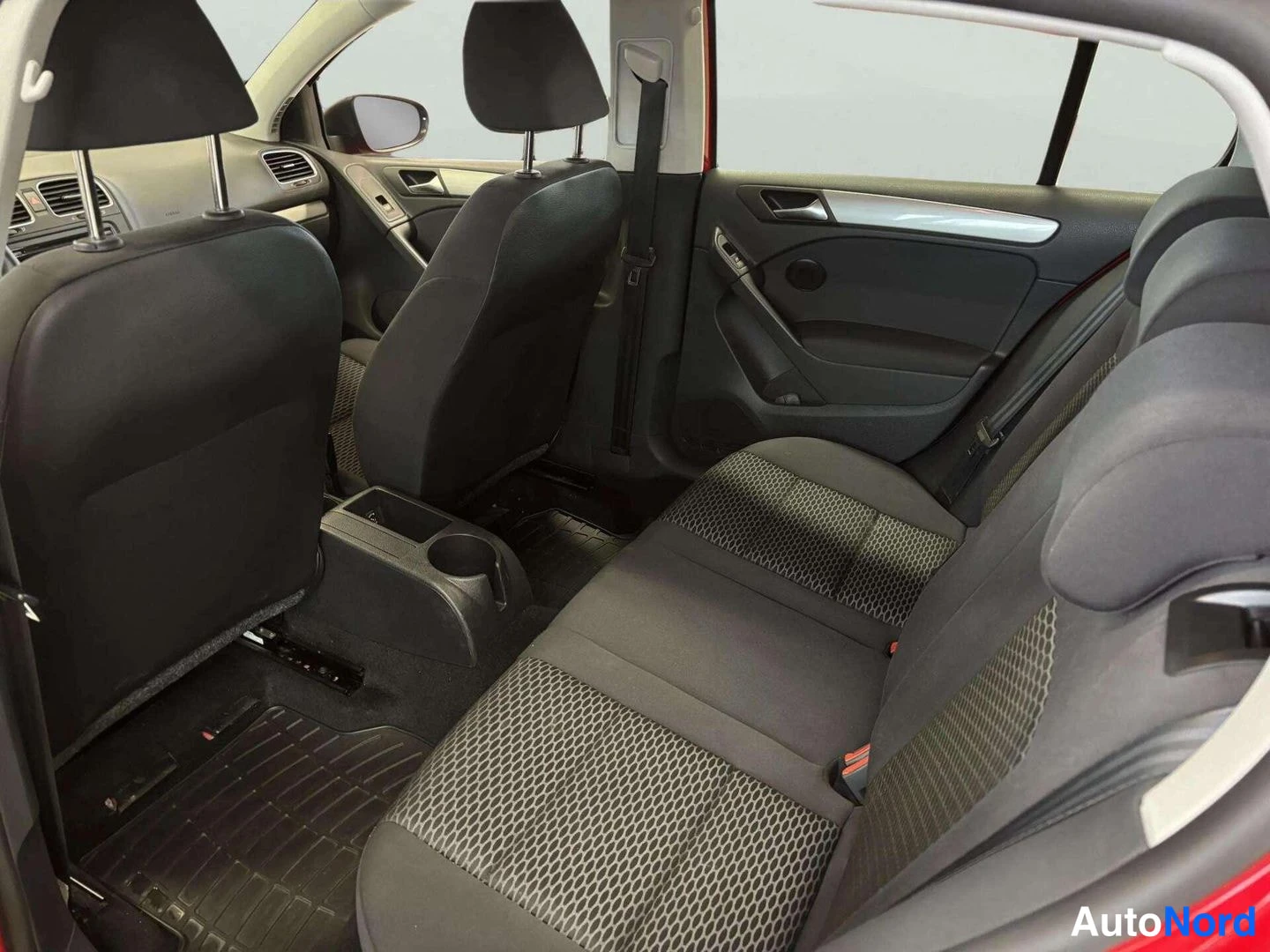 Muu: Volkswagen Golf -auton sisätila takaovi auki; näkyvissä takaistuin, etuistuinten selkänojat ja keskikonsoli, kuva tummat kangasistuimet ja punainen runkoviiva.