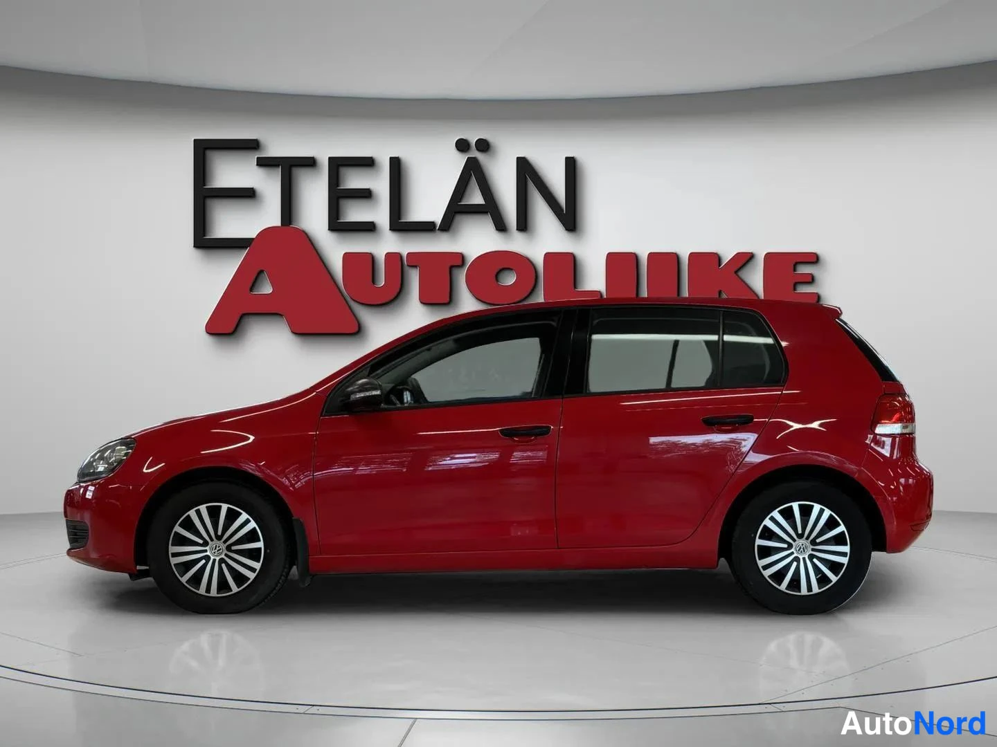 Sivulta: Punaisen Volkswagen Golfin sivunäkymä vasemmalta, täysi profiili showroomissa.