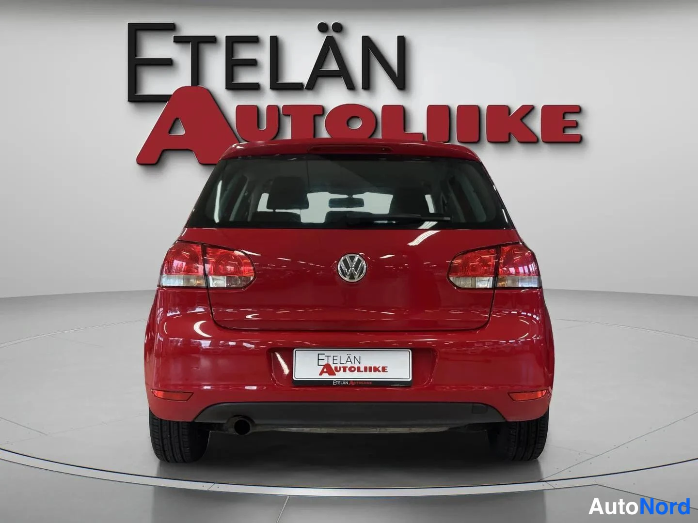 Takaa: Punainen viistoperäinen henkilöauto suoraan takaa studiossa; takavalot, VW-merkki ja rekisterikilpi näkyvät.