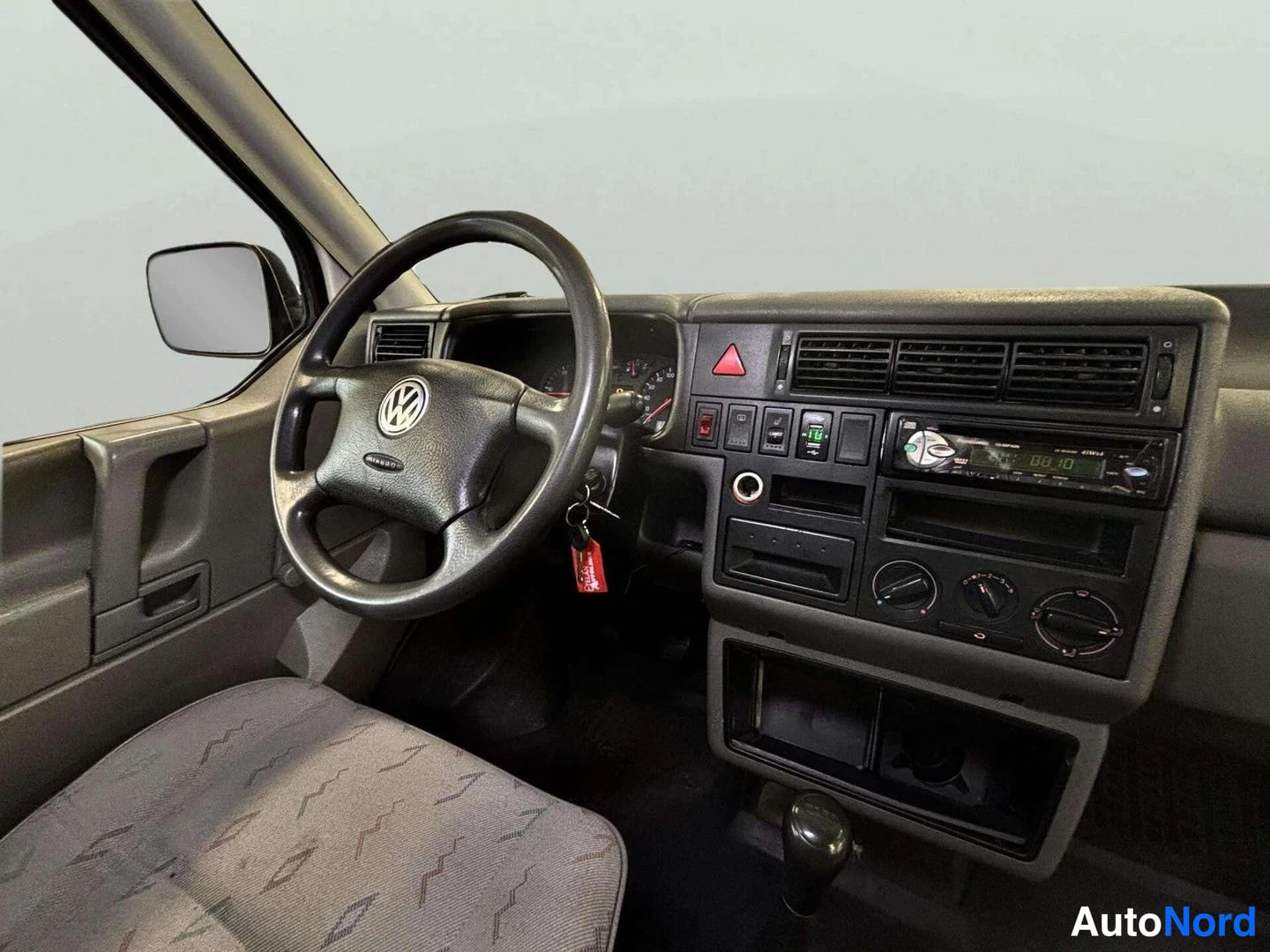 Muu: Auton kojelauta lähikuvassa: Volkswagen-ohjauspyörä, mittaristo, varoituskolmio ja radio, jonka näytöllä lukee 06.10.