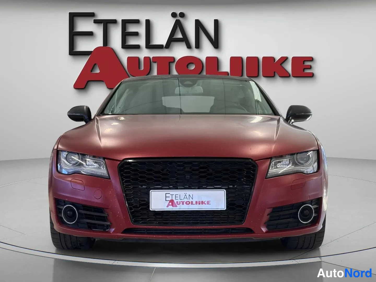 Edestä: Punaisen auton etunäkymä, musta konepelti ja etugrilli, Etelän Autoliike -logotietti taustalla.