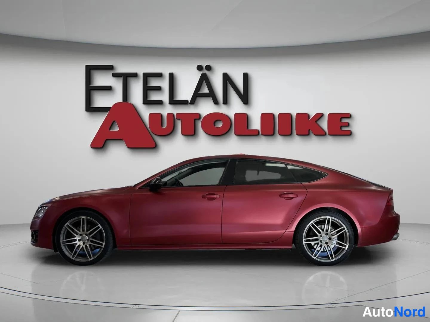 Sivulta: Punaisen auton sivunäkymä oikealta, viisiovainen coupe, kevytmetallivanteet.