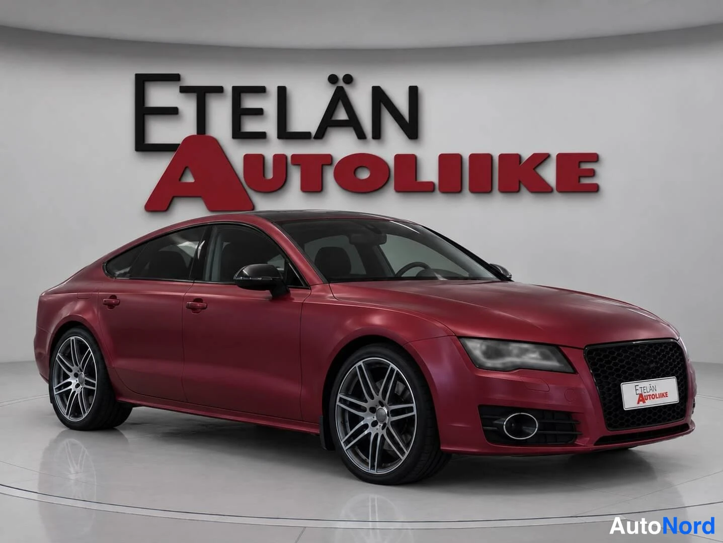 Etuviisto, nokka oikealle: Audi A7 -mallin tummanpunainen etukolmastonäkyvä auto studiotyttä kuvattuna, oikeaan kylkeen näkyvät hiilikuitu ilmakanava ja Etelä-Autoliikkeen wall-log