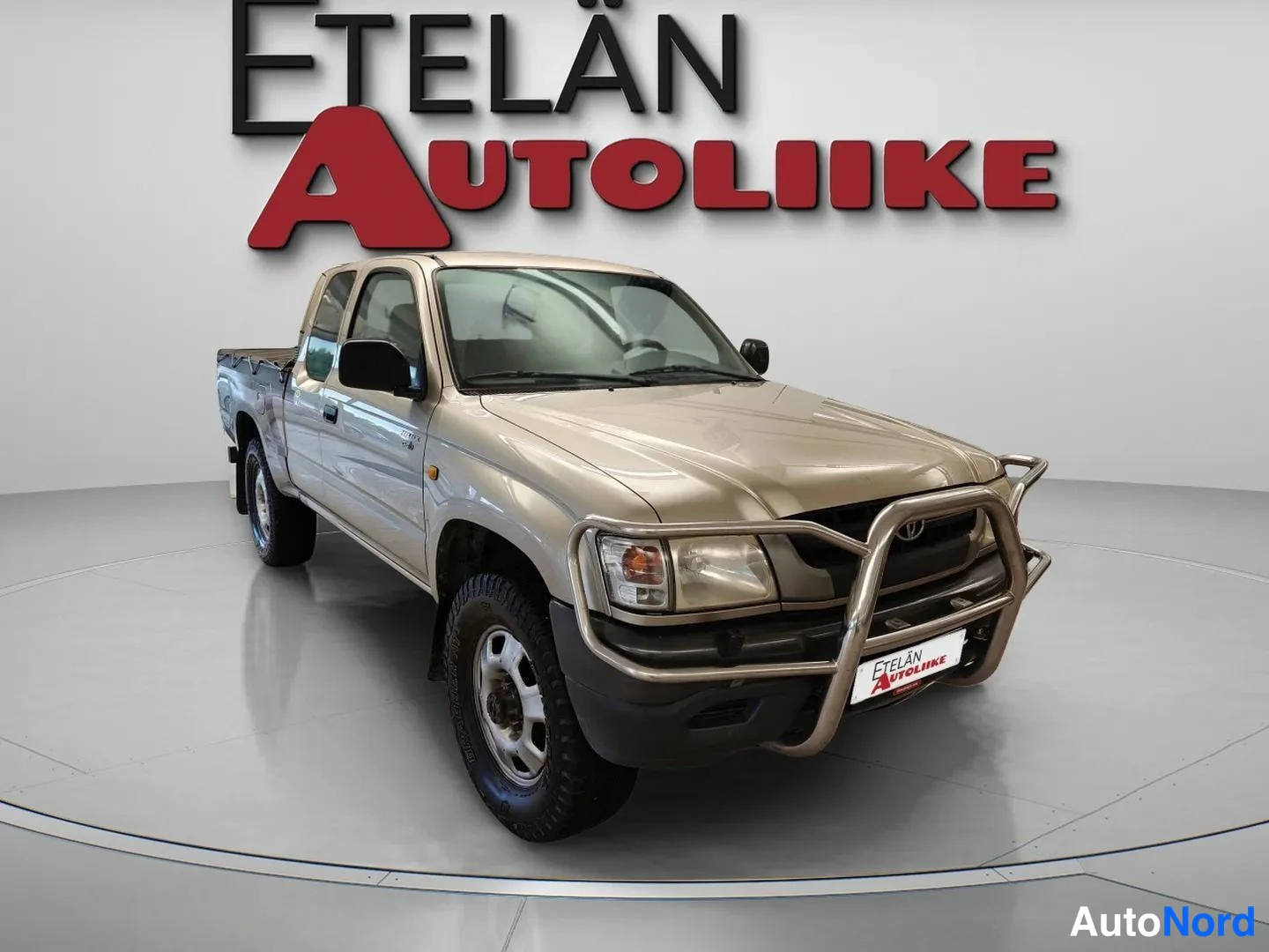 Etuviisto, nokka oikealle: Beige avolava-auto kulmassa edestä oikealta kuvattuna showroomissa.