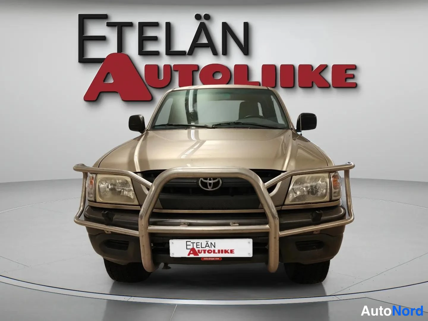 Edestä: Beige avolava-auto suoraan edestä kuvattuna showroomissa.
