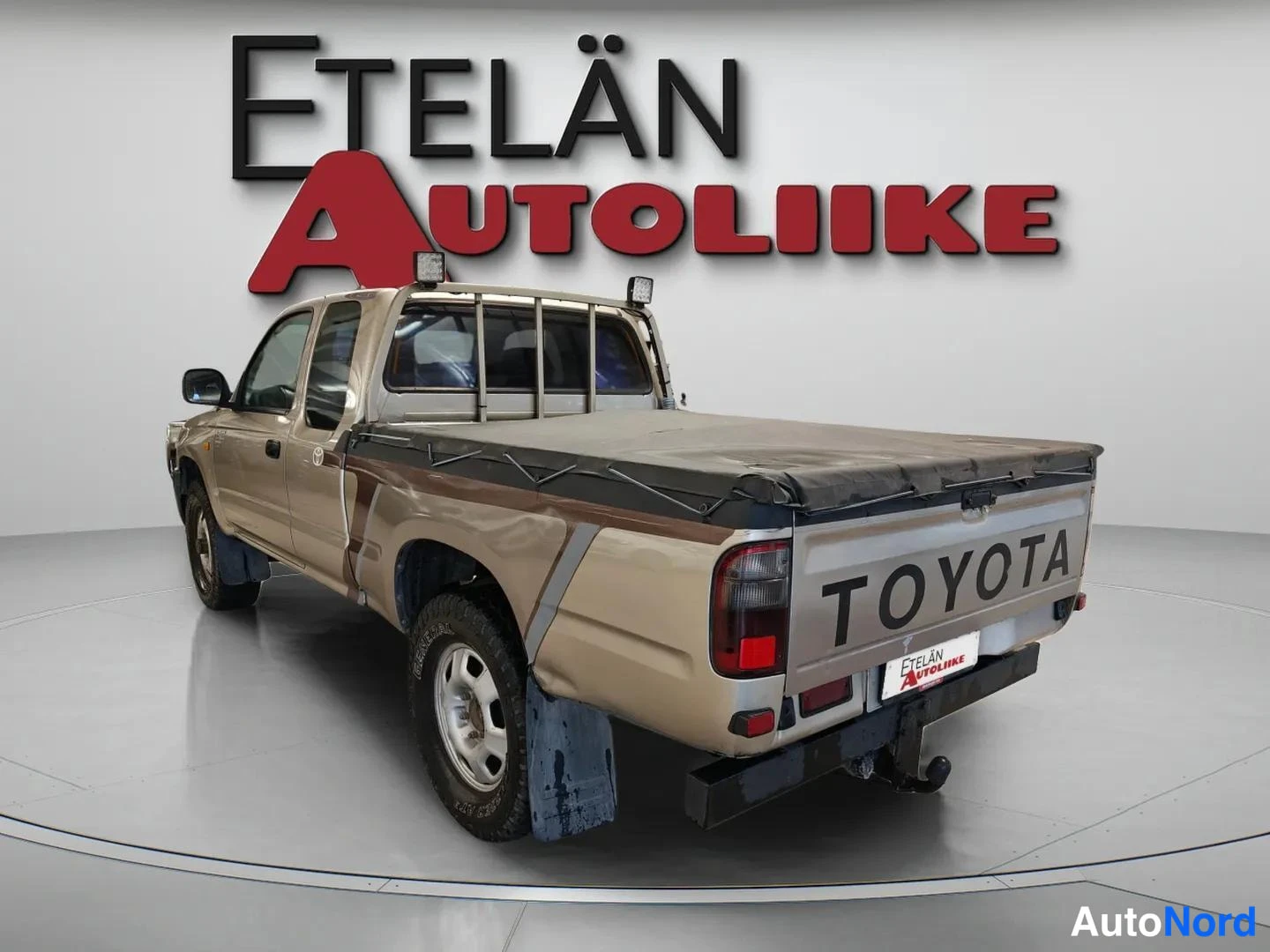 Takaviisto: Auton takakulman kissa, Toyota-pickup peitetyllä lavaosalla ja bokserikkeella.