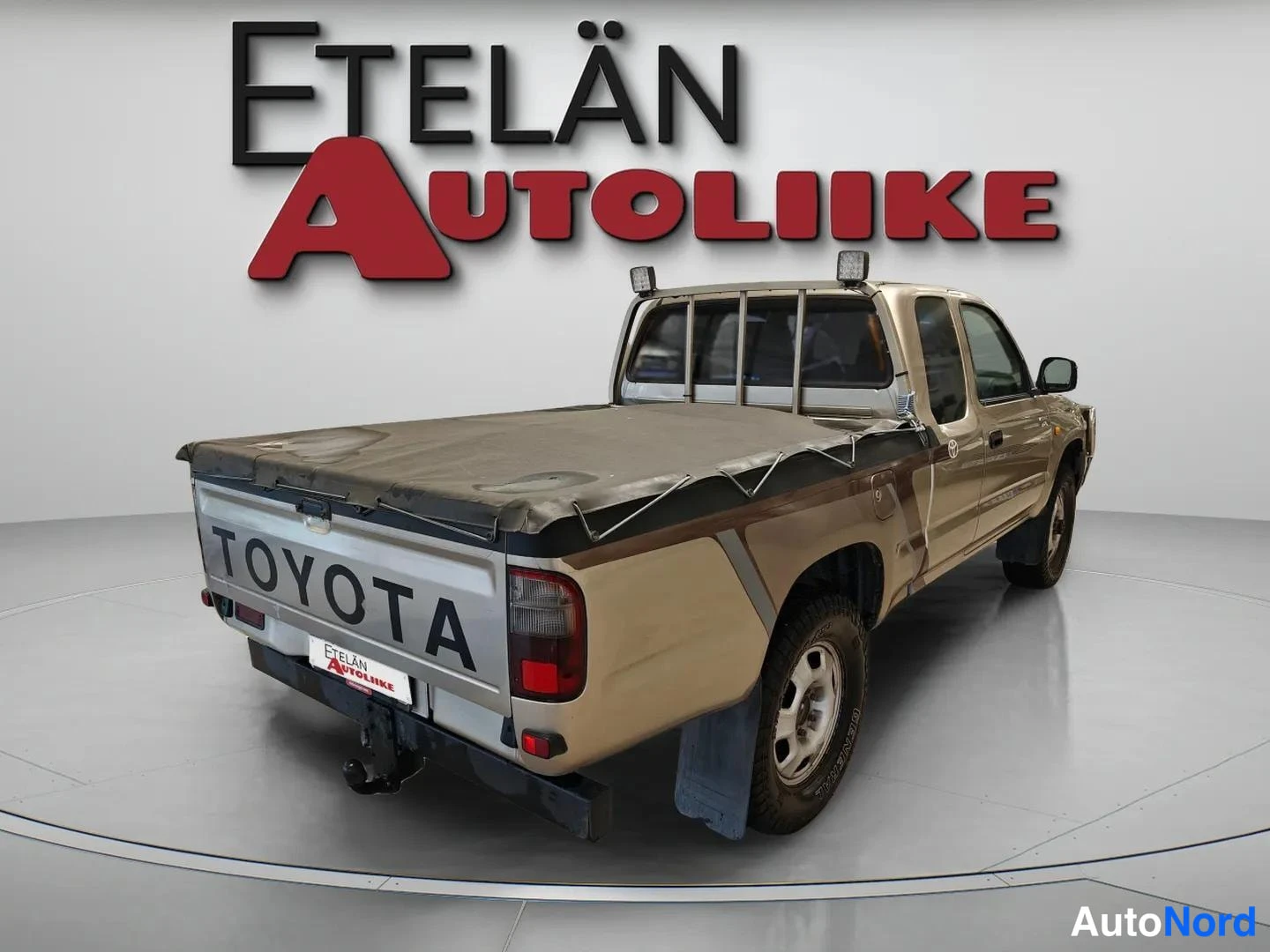 Takaviisto: Auton takakulman kissa vasemmalta, Toyota-pickup peitetyllä lavaosalla.