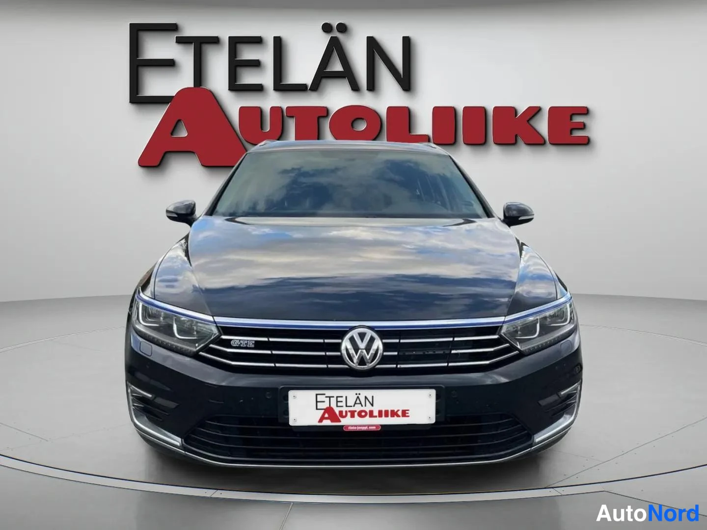 Edestä: Suora etunäkymä tummansinisestä Volkswagen-farmarista valokuvastiossa; etusäleikössä GTE-teksti ja sininen koristelista, Etelän Autoliike -mainostekstit kuvan y