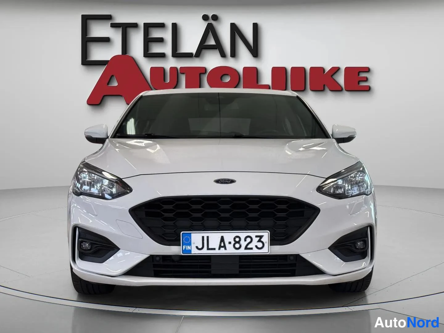 Edestä: Valkoisen auton etunäkökuvassa rekisterikilpi lukee, taustalla mainos ETELÄN AUTOLIIKE.