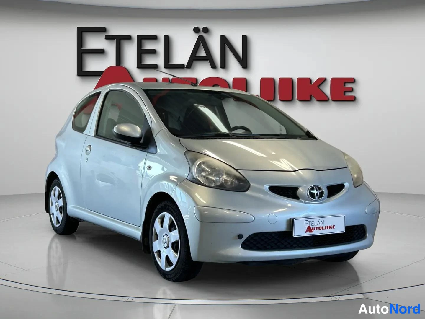 Etuviisto, nokka oikealle: Front three-quarter view of a silver two-door Toyota Aygo from the left side.