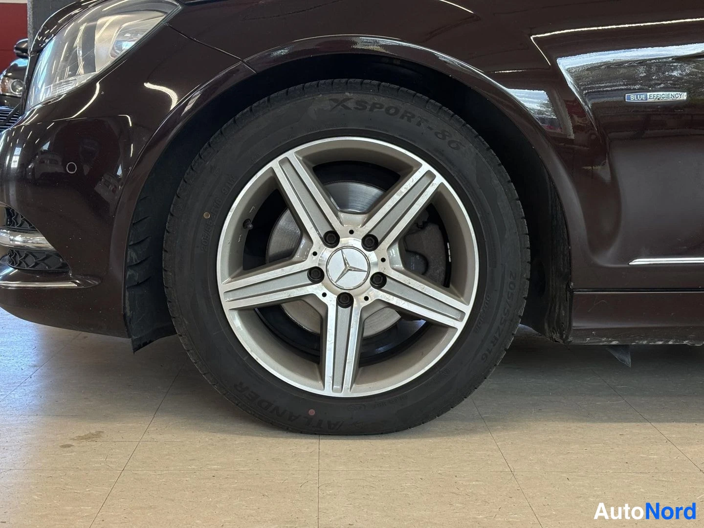 Yksityiskohta: Etupyörä lähikuvana. Viisisäteinen hopeainen kevytmetallivanteet, Mercedes-tähtilogo. Kumin kyljessä merkit „Xsport 80”. Sivuosassa embleemi „BLUE EFFICIENCY”.