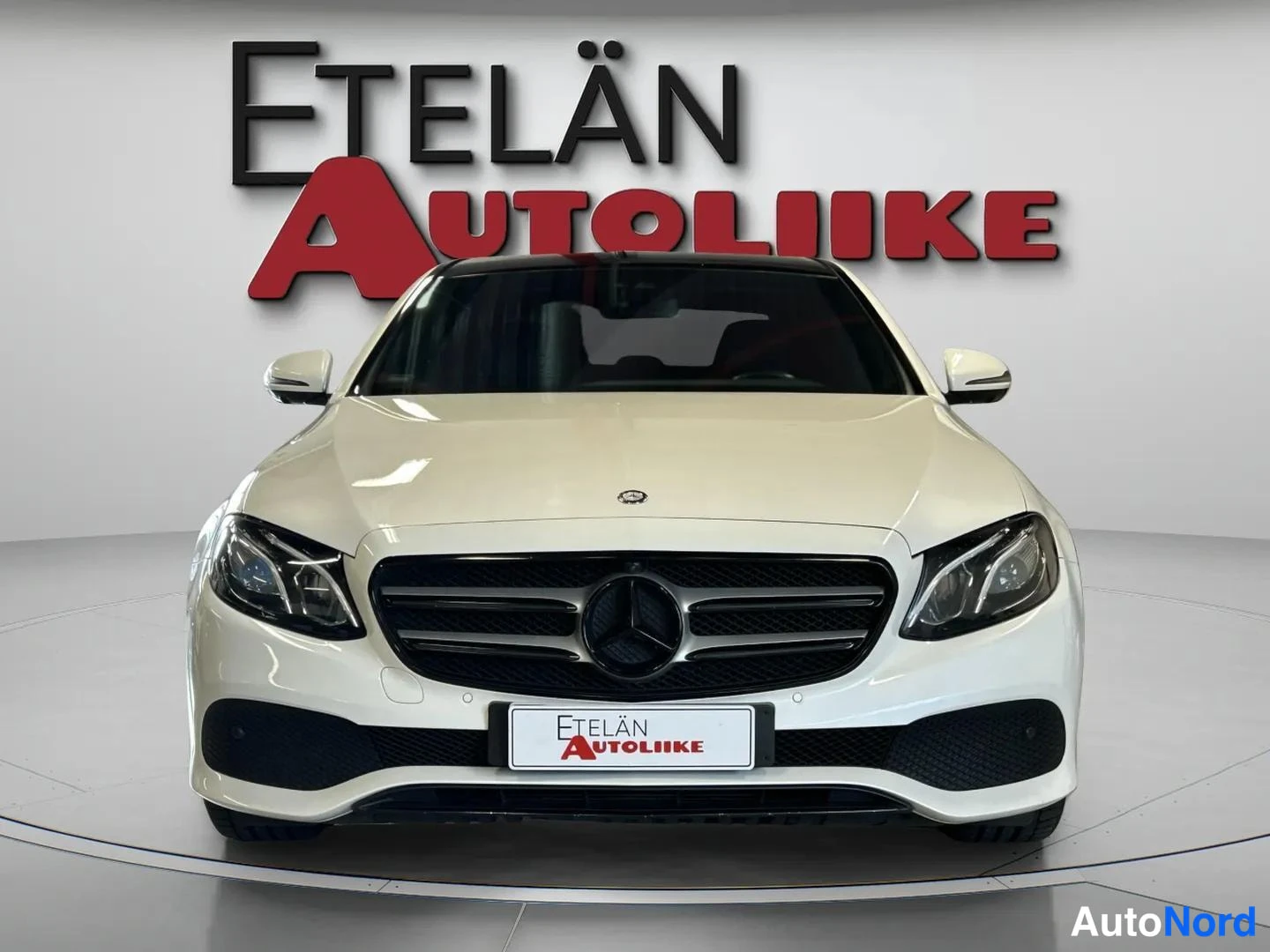 Edestä: Valkoinen Mercedes-Benz sedan suoraan edestä, musta etusäleikkö ja Mercedes-tähti.