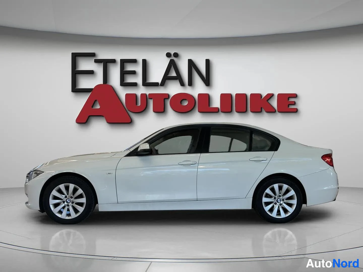 Sivulta: Side profile of a white four-door BMW showing both doors, windows, wheels and tinted glass along the full length
