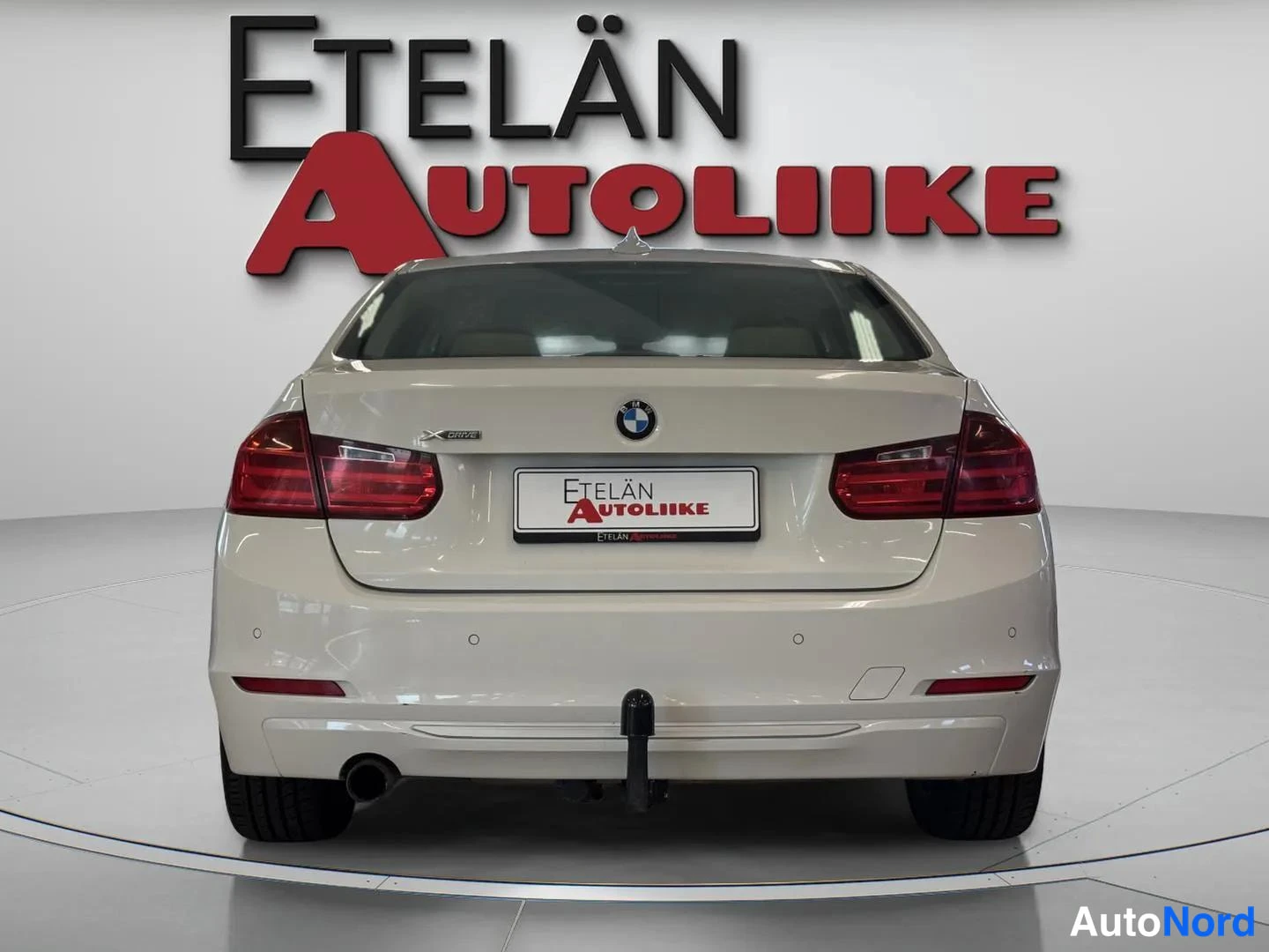 Takaa: Auton takaosa suoraan takaa; valkoinen sedan, punaiset takavalot, BMW-merkki pakovalta ja Vetelin Autoliike -kyltti.