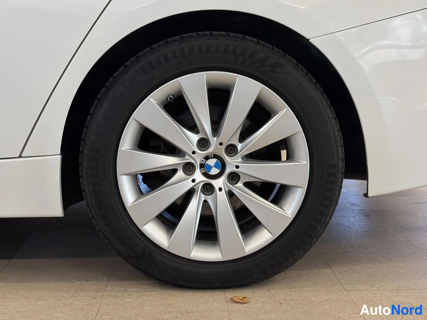 Sivulta: Valkoinen auton runko ja kromattu 18 tuuman kevytmetallivannettu takapyörä BMW-tunnuksella; rengas merkitty Nokian.