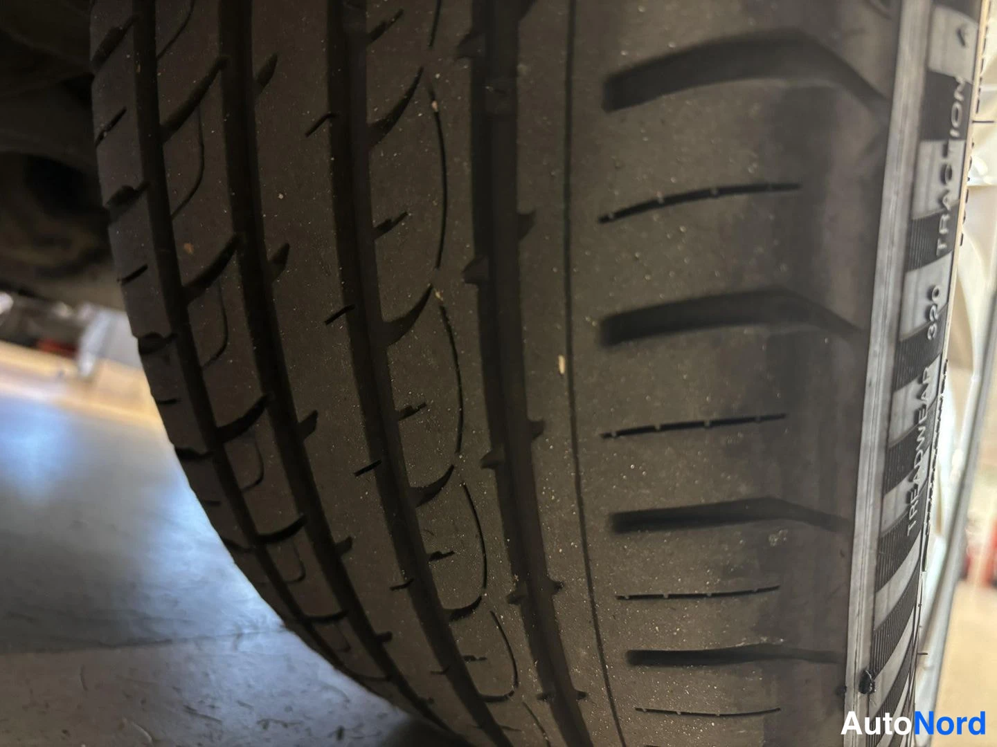 Sivulta: Lähikuva auton mustasta kesärengasta, jonka urat ja sivuseinän TREADWEAR 320 TRACTION A -merkinnät näkyvät tarkasti.