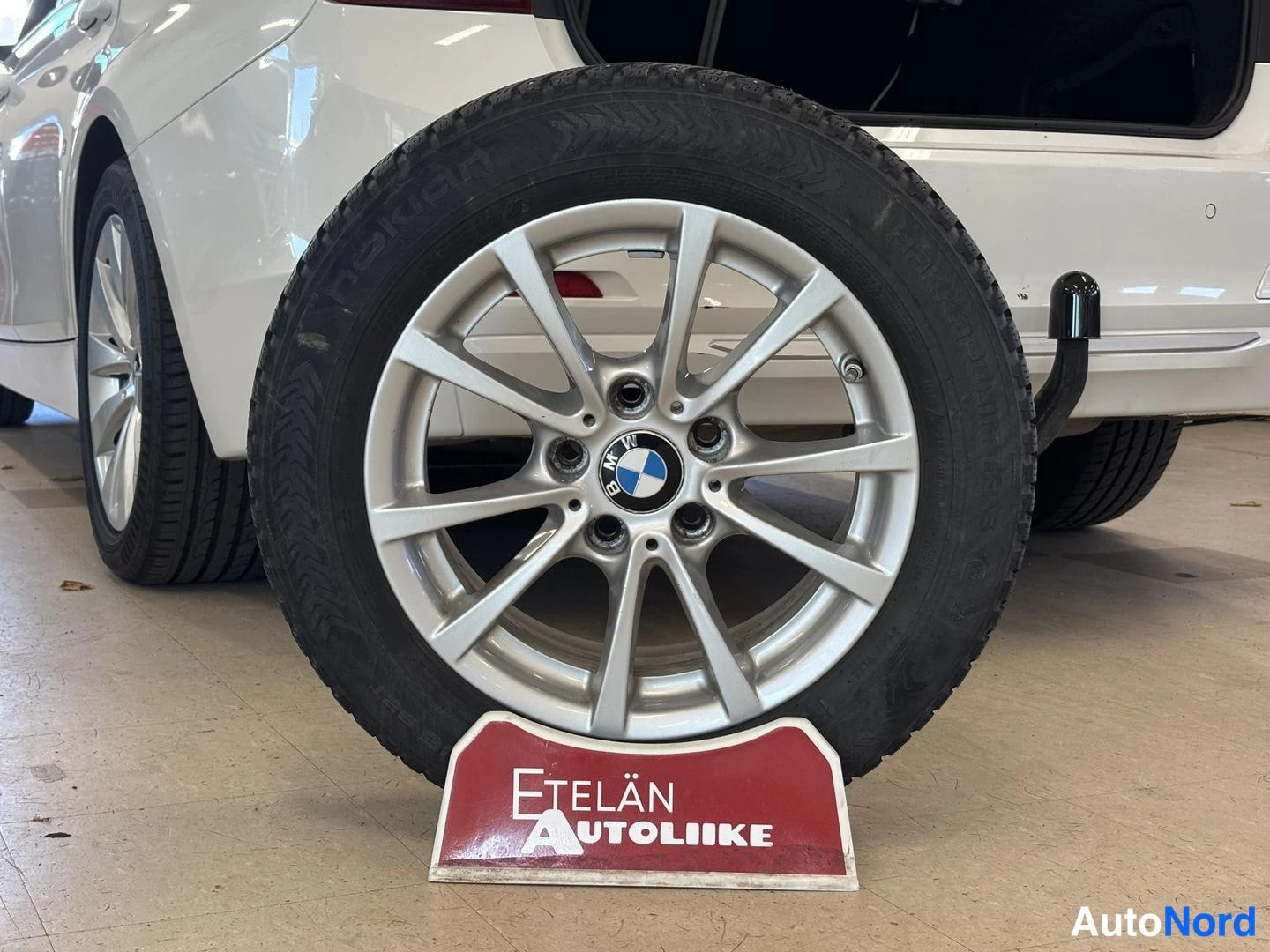 Takaviisto: Valokuvassa näkyy auton takapää ja nokkakoukku taustalla; edessä rekassa on Nokian talvirengas BMW-kevytmetallivanteella, ja kyltin Etelän Autoliike.