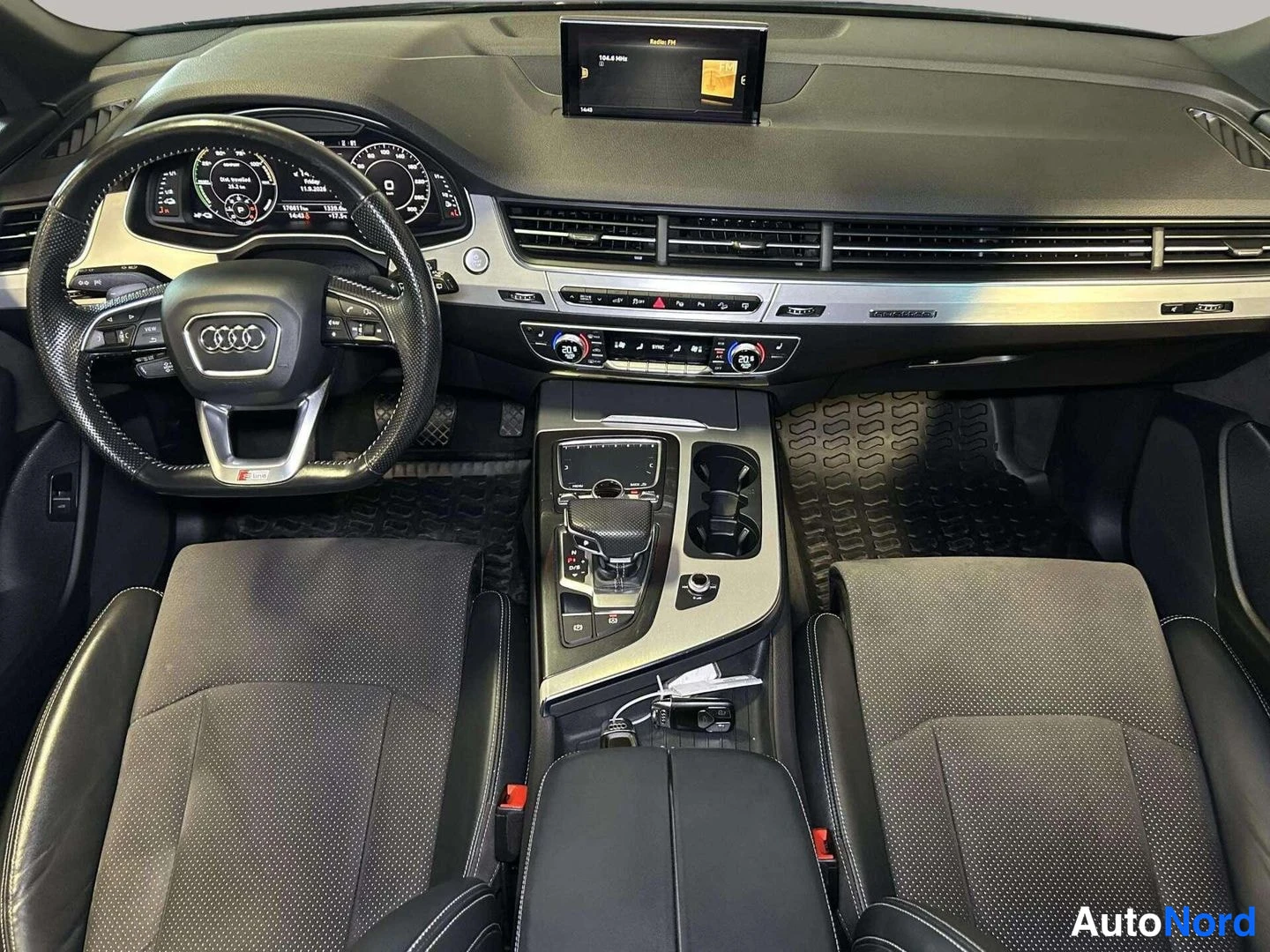 Edestä: Audi Q7:n kojelauta suoraan edestä kuvattuna: Audi-ohjauspyörä, näyttö ja kaksi etuistuinta näkyvissä.