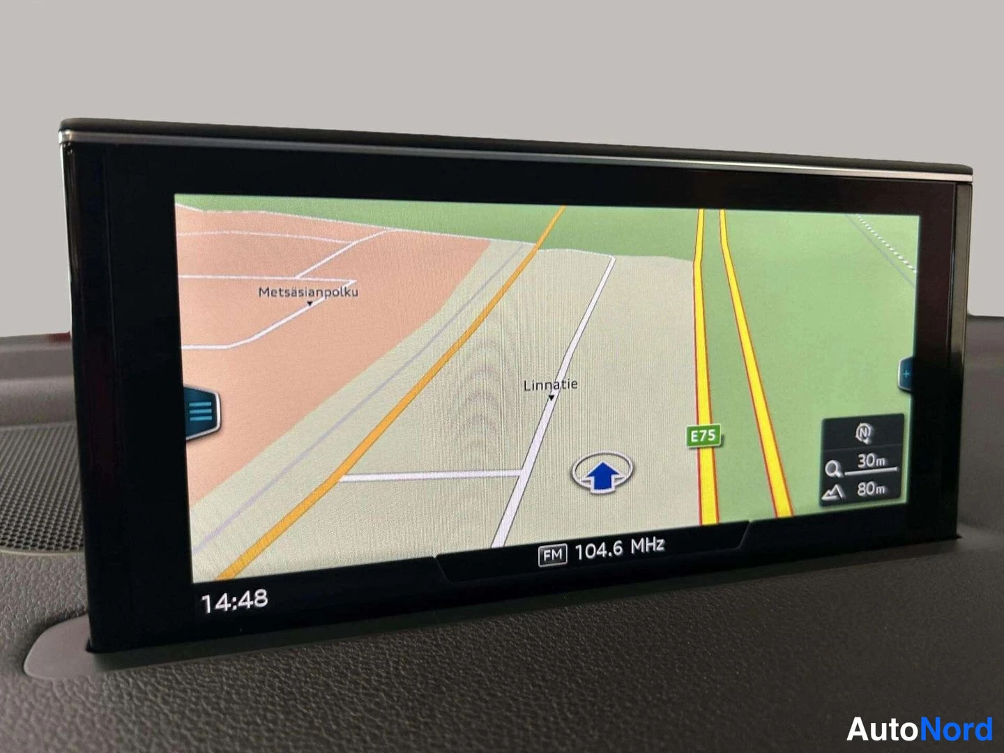 Yksityiskohta: Audi Q7:n kojelaudan infotainment-näyttö näyttää navigointikartan reittiohjeineen ja radiokanavana FM 104.6 MHz.
