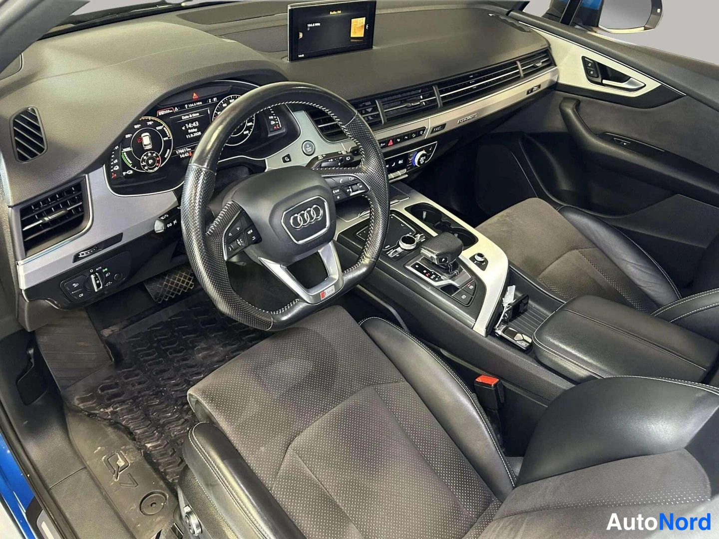 Edestä: Audi Q7:n sisätilat ohjaamon ovesta kuvattuna: Audi-ohjauspyörä, digitaalinen mittaristo ja keskikonsoli näkyvissä.