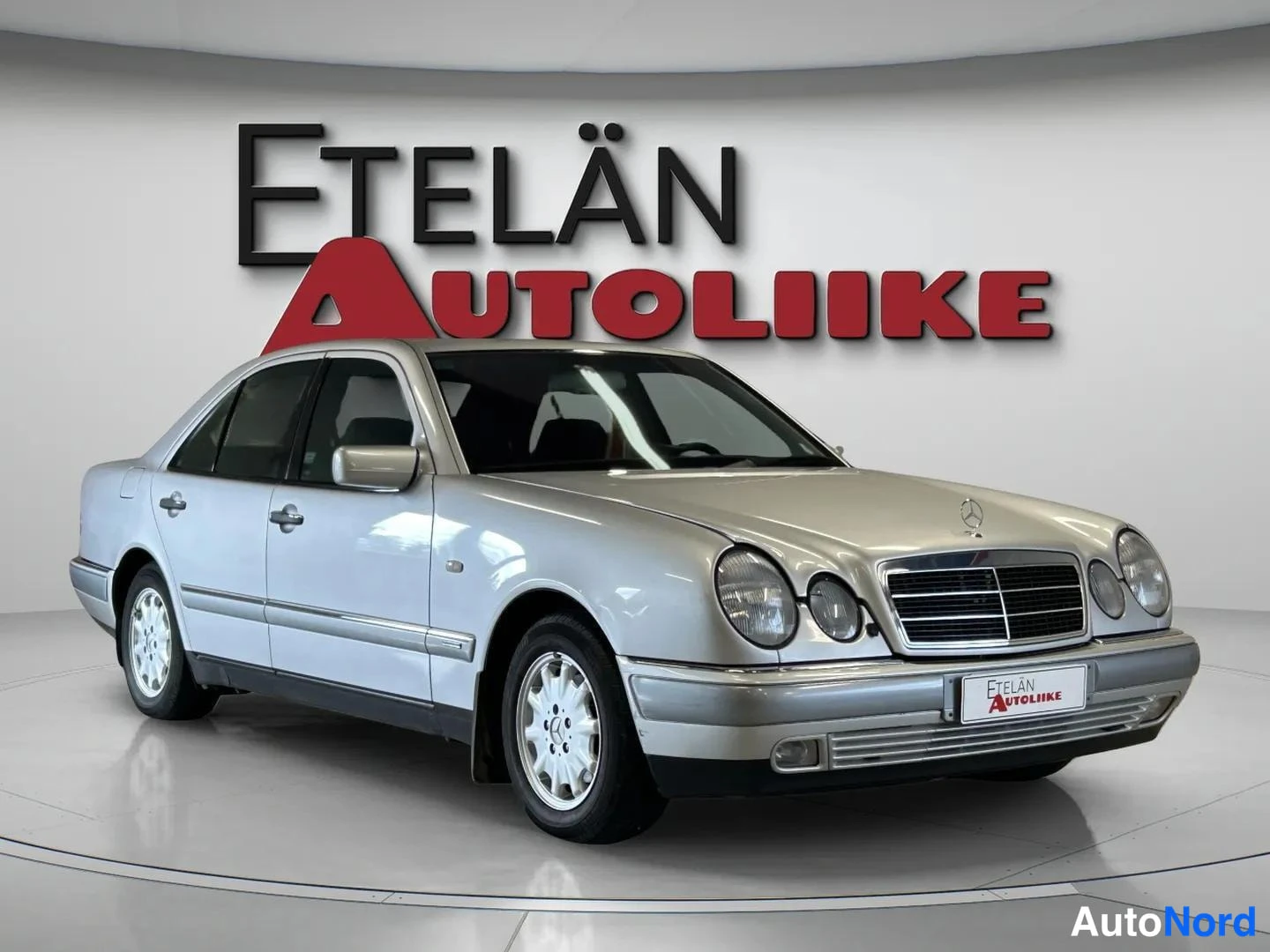 Etuviisto, nokka oikealle: Hopeanvärinen Mercedes-Benz-sedan kolmella neljäsosasta kuvattuna keulasta oikealta, pyörällä studiossa.