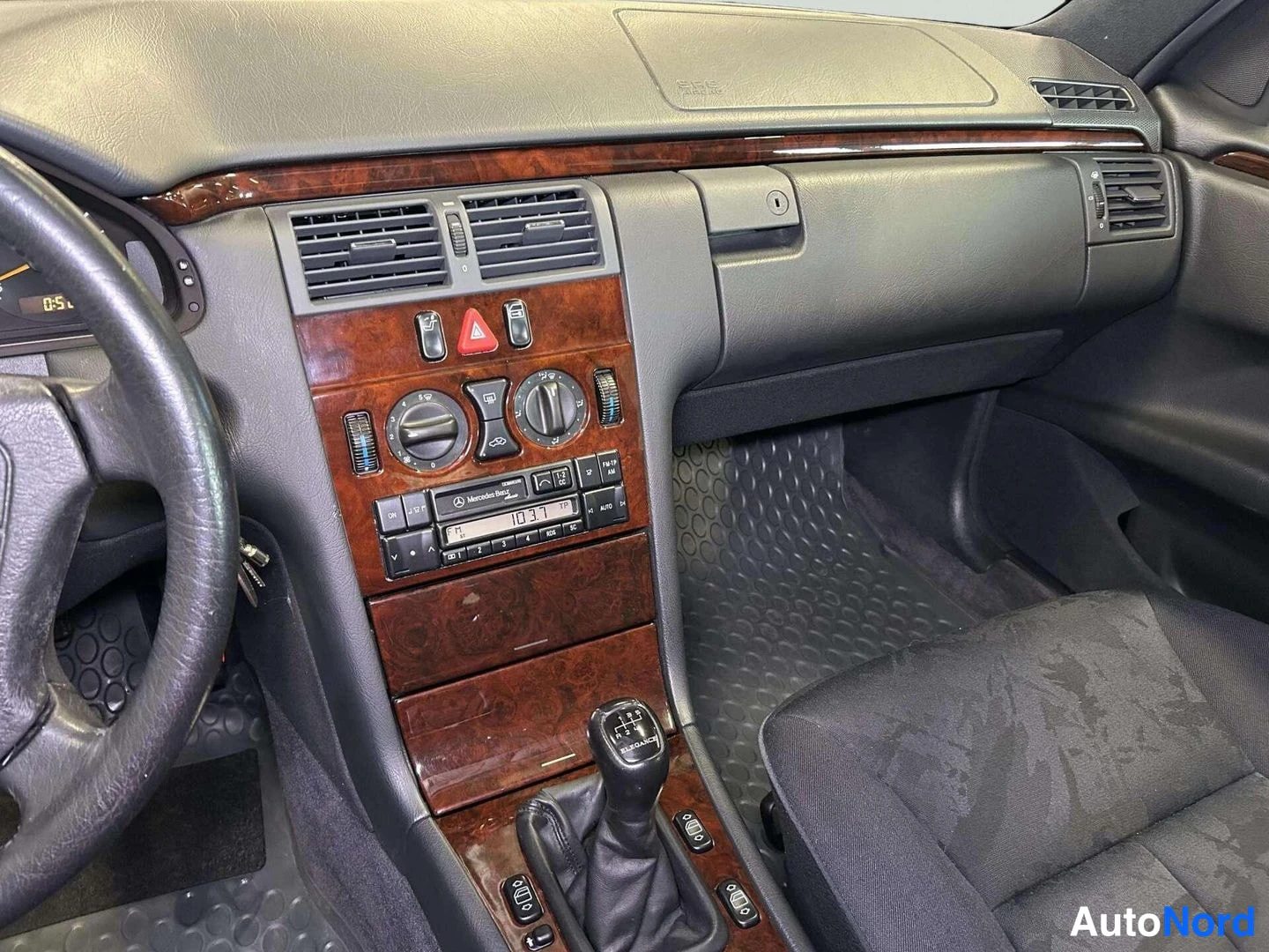 Edestä: Sisäkuva: Mercedes-Benzin keskikonsoli puidoitetuine paneeleineen, ilmastoinnin pyörösäätimet, Mercedes-Benz Classic -radio näytöllä 103.7 ja vaihtajanoppa; koj