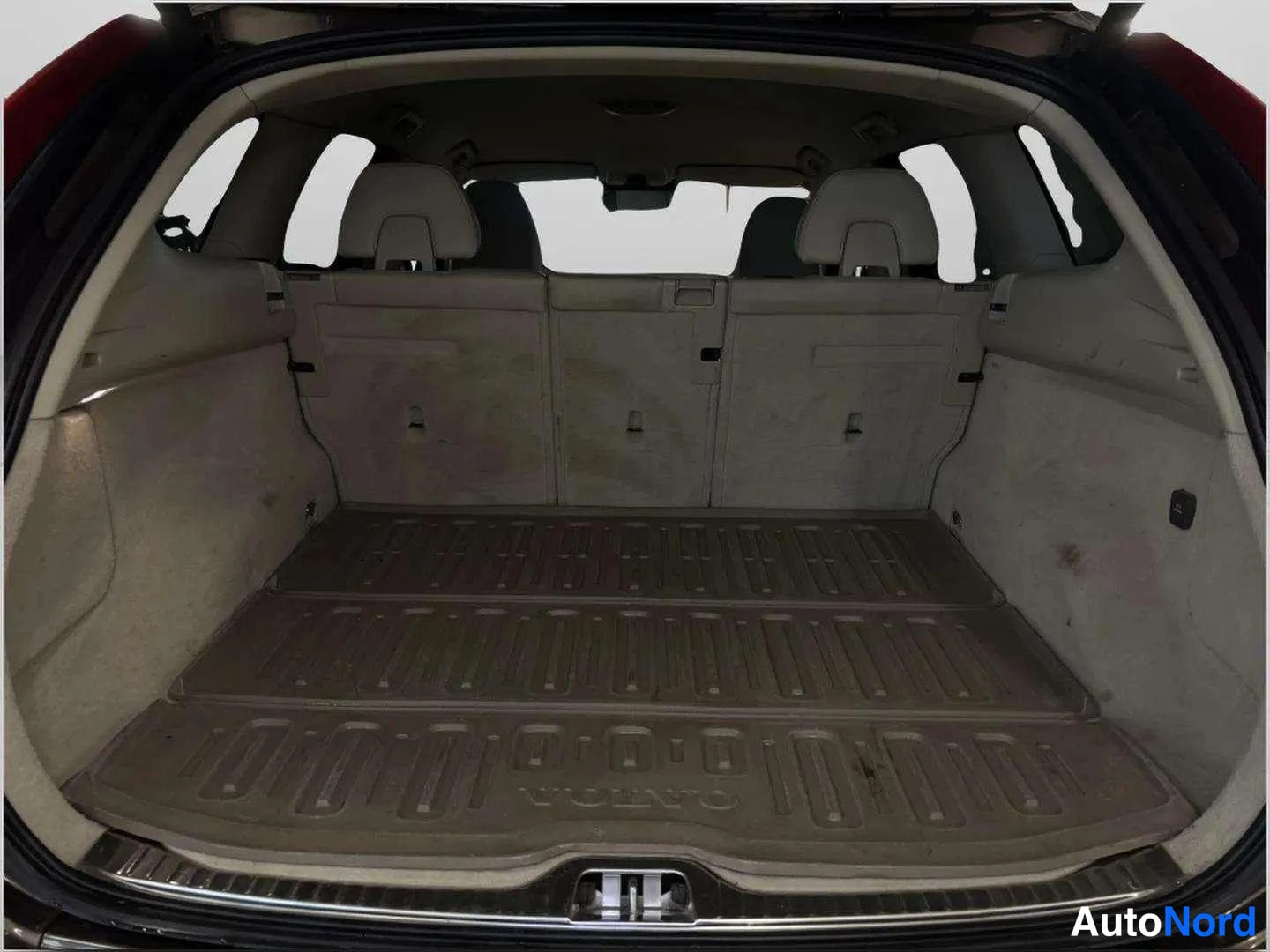 Takaistuimet: Auton avattu tavaratila, jossa tumma muovimatto ja taitettuna takaselkänojat; Volvo-teksti mattossa.