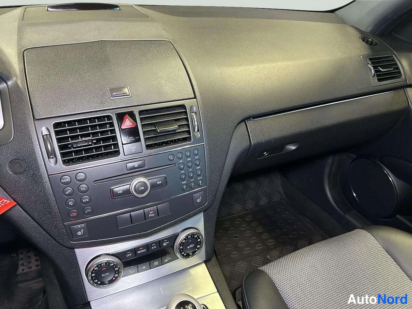 Muu: Keskikonsolin lähikuva: radio, painikkeet ja automaattinen ilmastointi (A/C, AUTO), matot ja osa istuimesta.