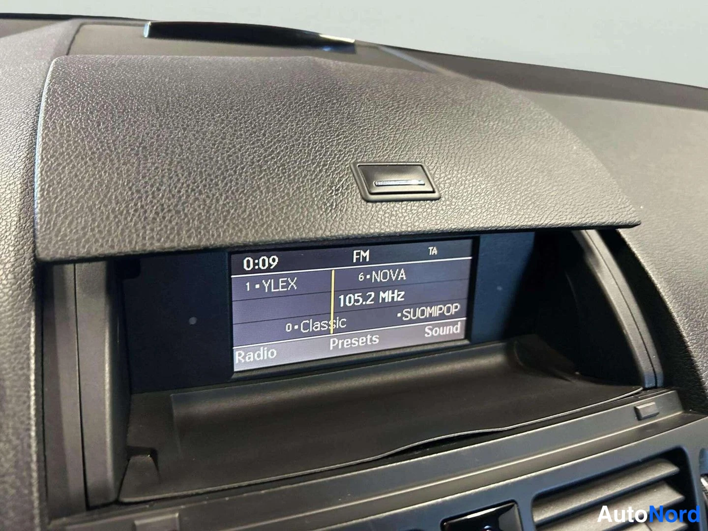 Muu: Ajomittarin näytön lähikuva: kello 0:09, FM 105.2 MHz, kanava 6 NOVA.
