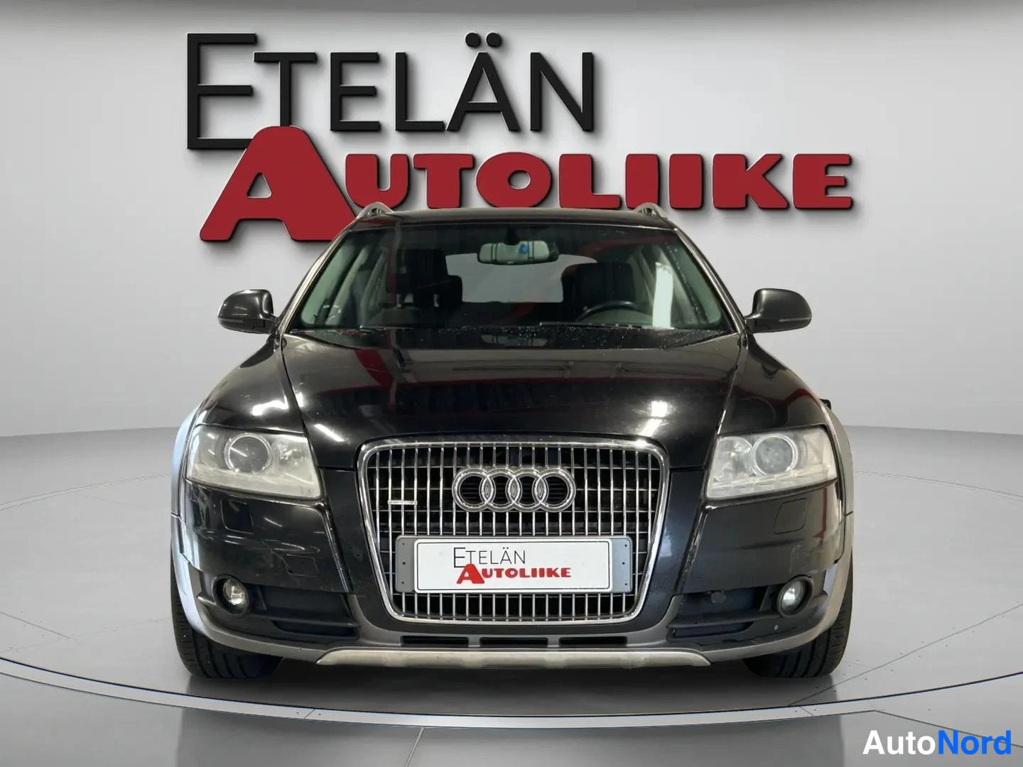 Edestä: Mustan Audi A4:n etunäkymä studiovaaleaa taustaa vasten; etusäleikössä Audi-logot, kattoon asennetut kaarit, kuvassa myyjän logo Etelän Autoliike.