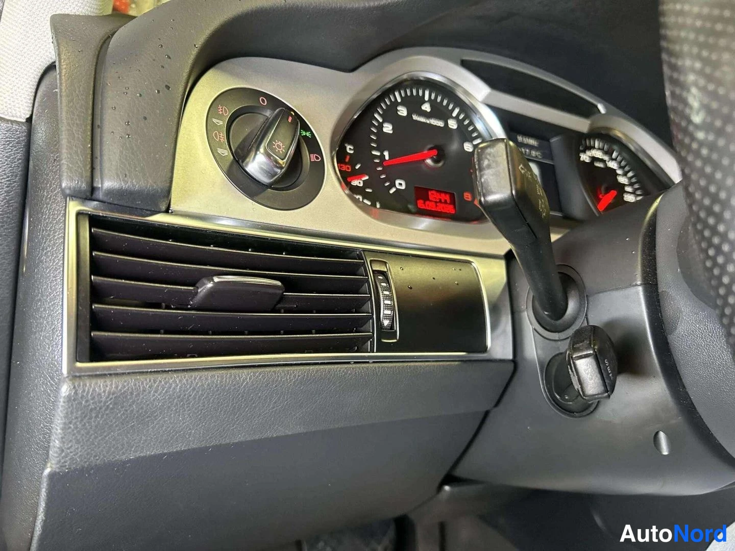 Muu: Audi A4:n kojelaudan vasen osa: pyörivä valaistussäädin, ilmastointiritilä ja mittariston osa punaisella näytöllä.