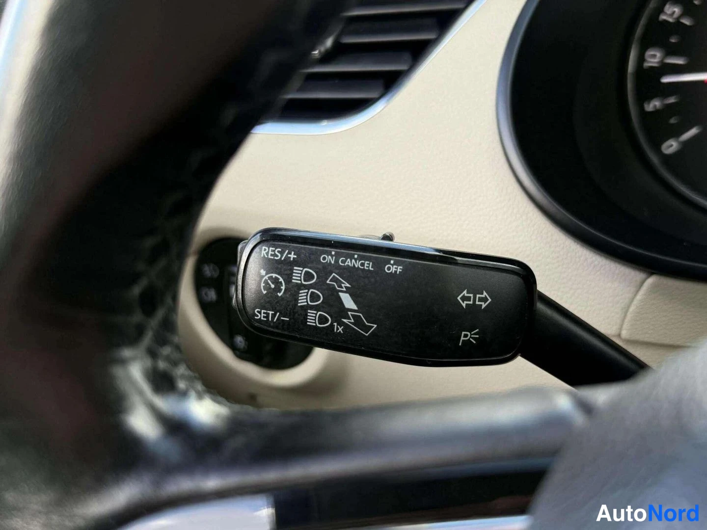 Yksityiskohta: Ohjauspyörän takainen ohjausvipu lähikuvassa, tekstit RES/+, SET/-, ON, CANCEL ja OFF; cruise control -toiminto.