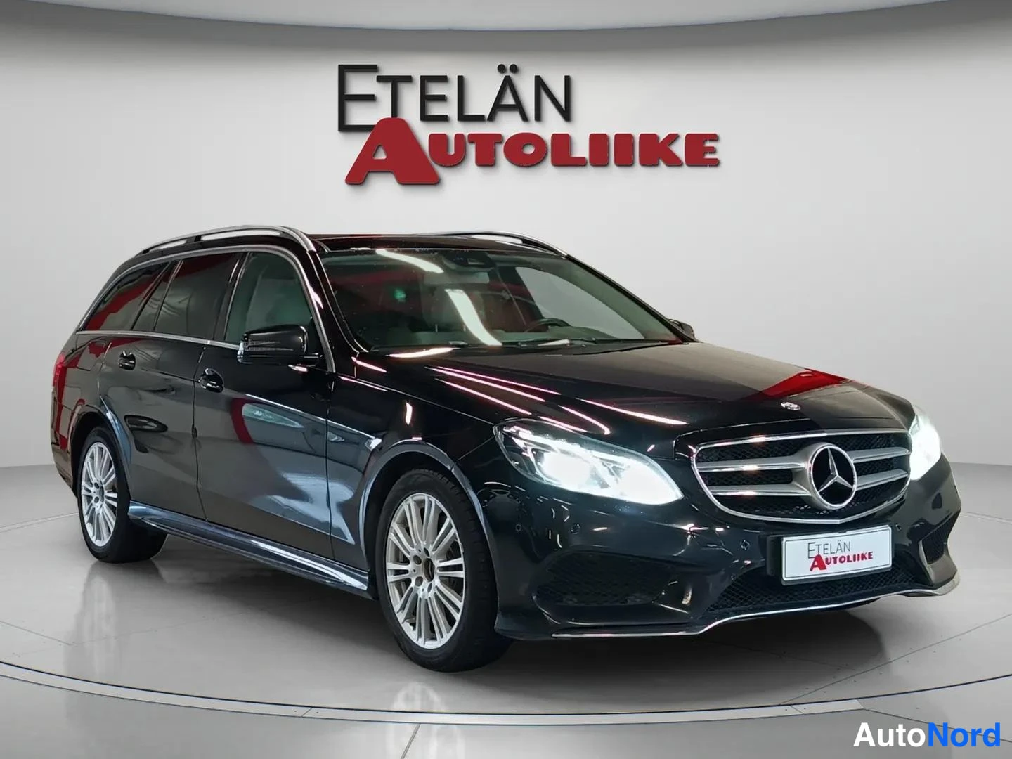 Etuviisto, nokka oikealle: Etelaen Autoliike -logon alla tumma farmarimallinen Mercedes-Benz etuviistosta kuvattuna