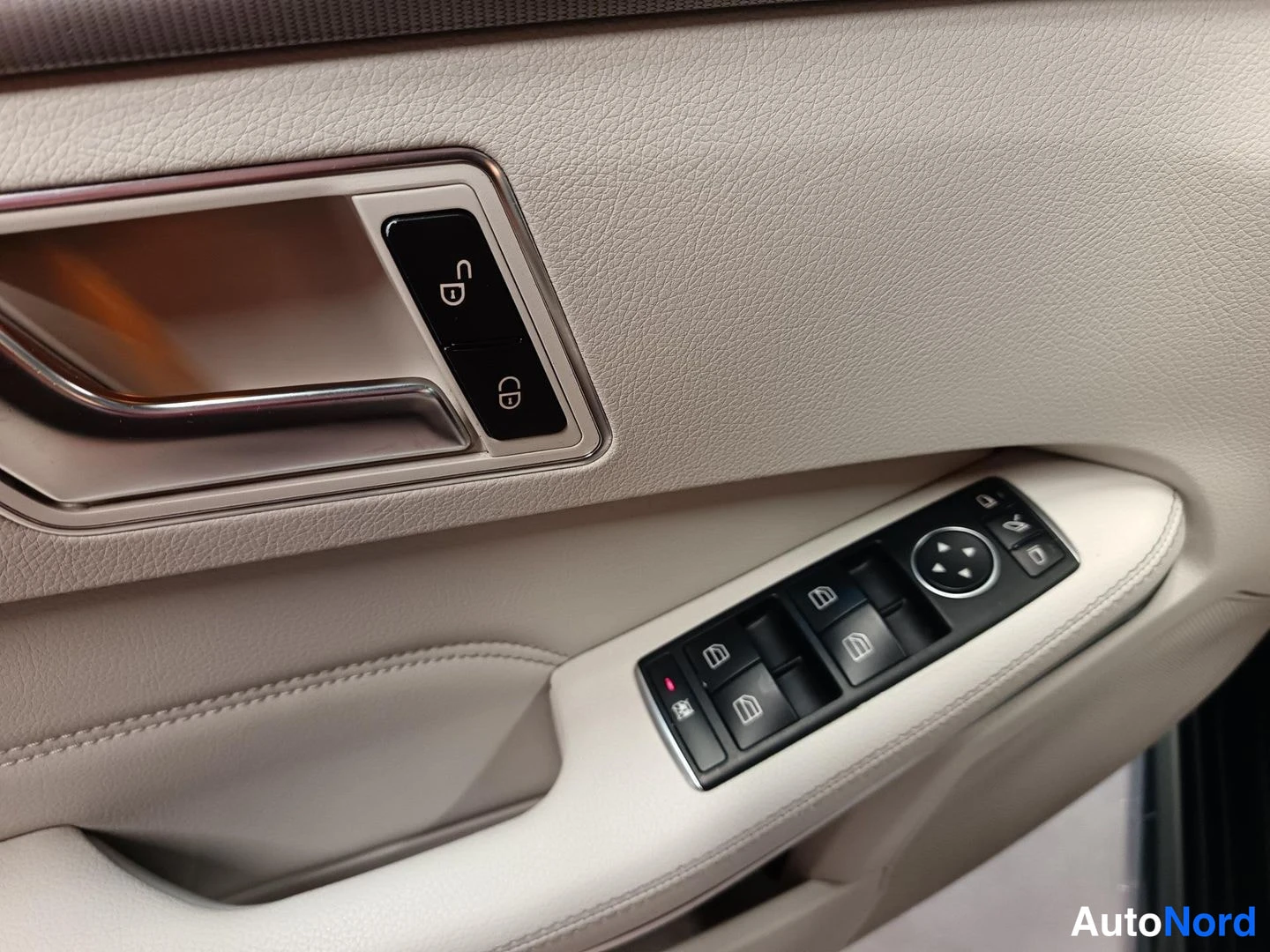 Ohjaamo: View of the driver's door interior in beige leather with a chrome grab handle. A button cluster above contains mirror controls, while a lower panel shows switch