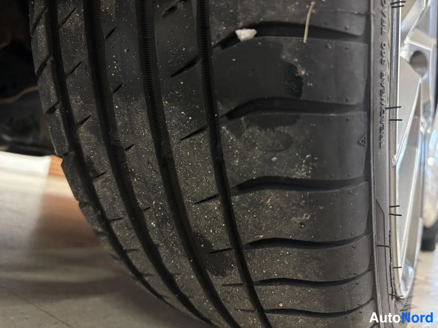 Muu: Erityisen lähikuva auton renkaasta: kulutuspinnan urat ja rengassivun merkinnät, muun muassa TREADWEAR 320.
