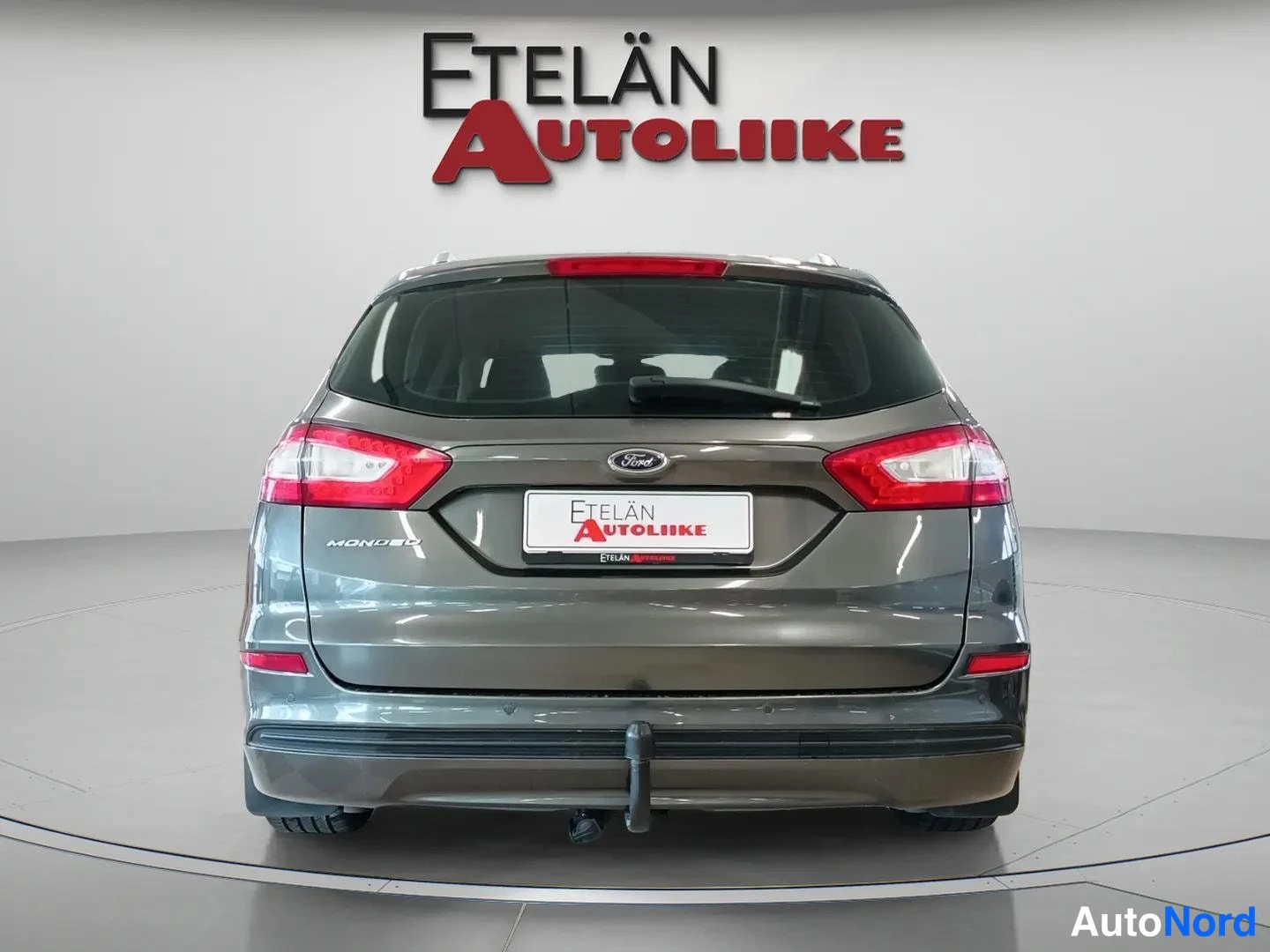 Takaa: Suora takanäkymä harmaasta farmariautosta: punaiset takavalot, Ford-merkki, Mondeo-teksti ja vetokoukku.