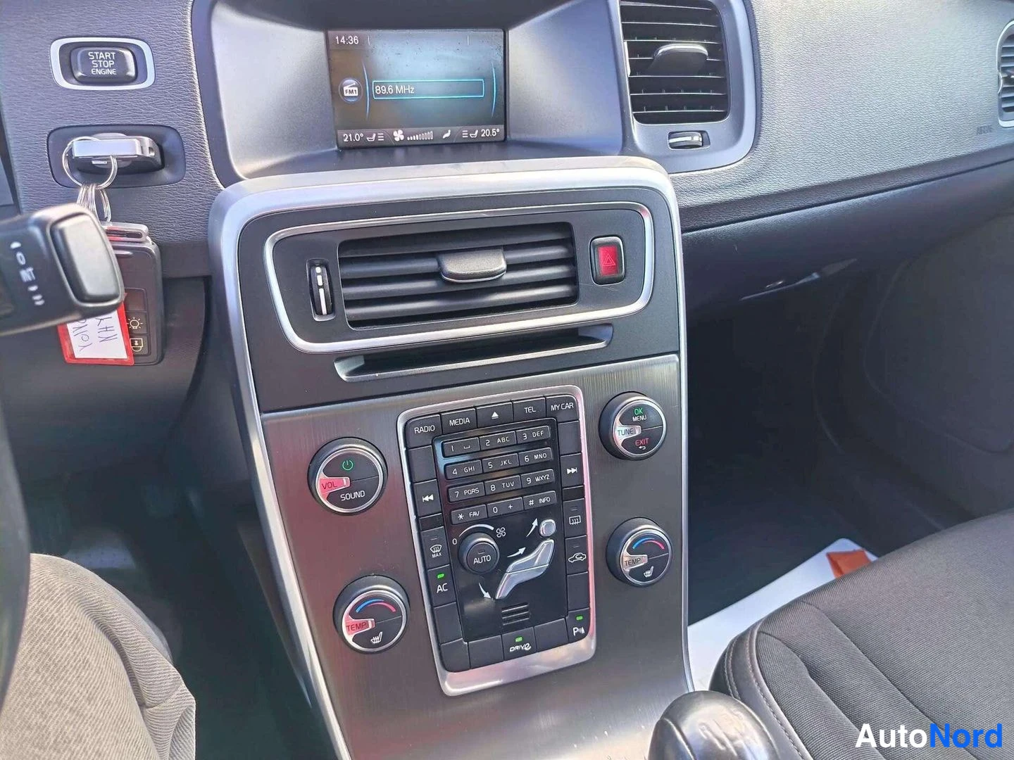 Muu: Volvo S80:n kojelauta: keskikonsoli, radio näytöllä 89.6 MHz, ilmastointipainikkeet AC ja AUTO, START/STOP ENGINE -painike ja avaimet sytytyslukossa.