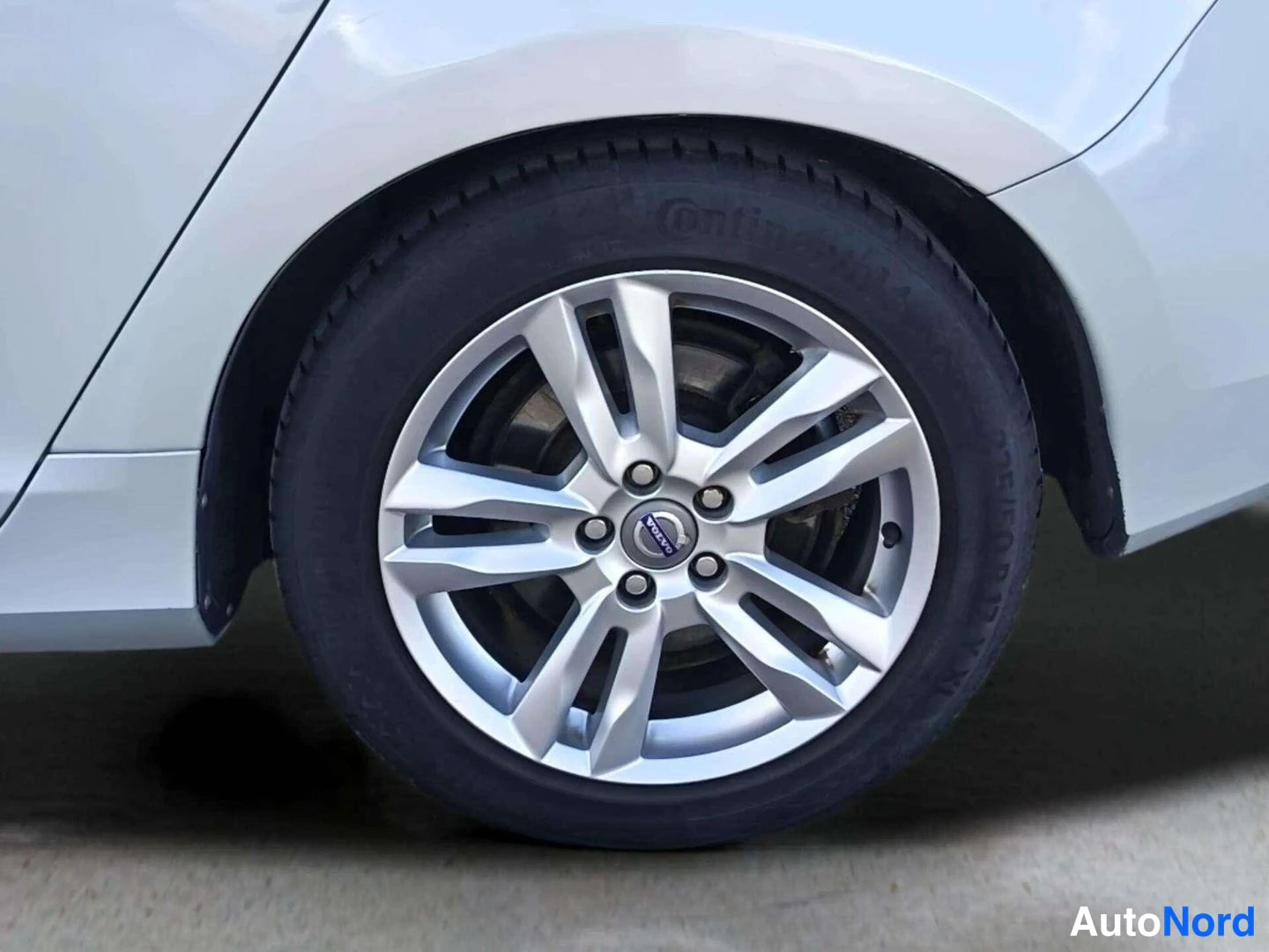 Muu: Valkoisen auton etupyörän lähikuva: hopeanvärinen Volvo-vanne ja Continental-renkaat.