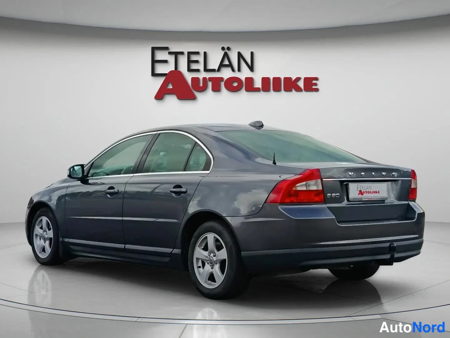 Takaviisto: Auton takanurkkakuva studio-olosuhteissa, tummanharmaa sedan, taustavalot ja takapuskuri näkyvissä.