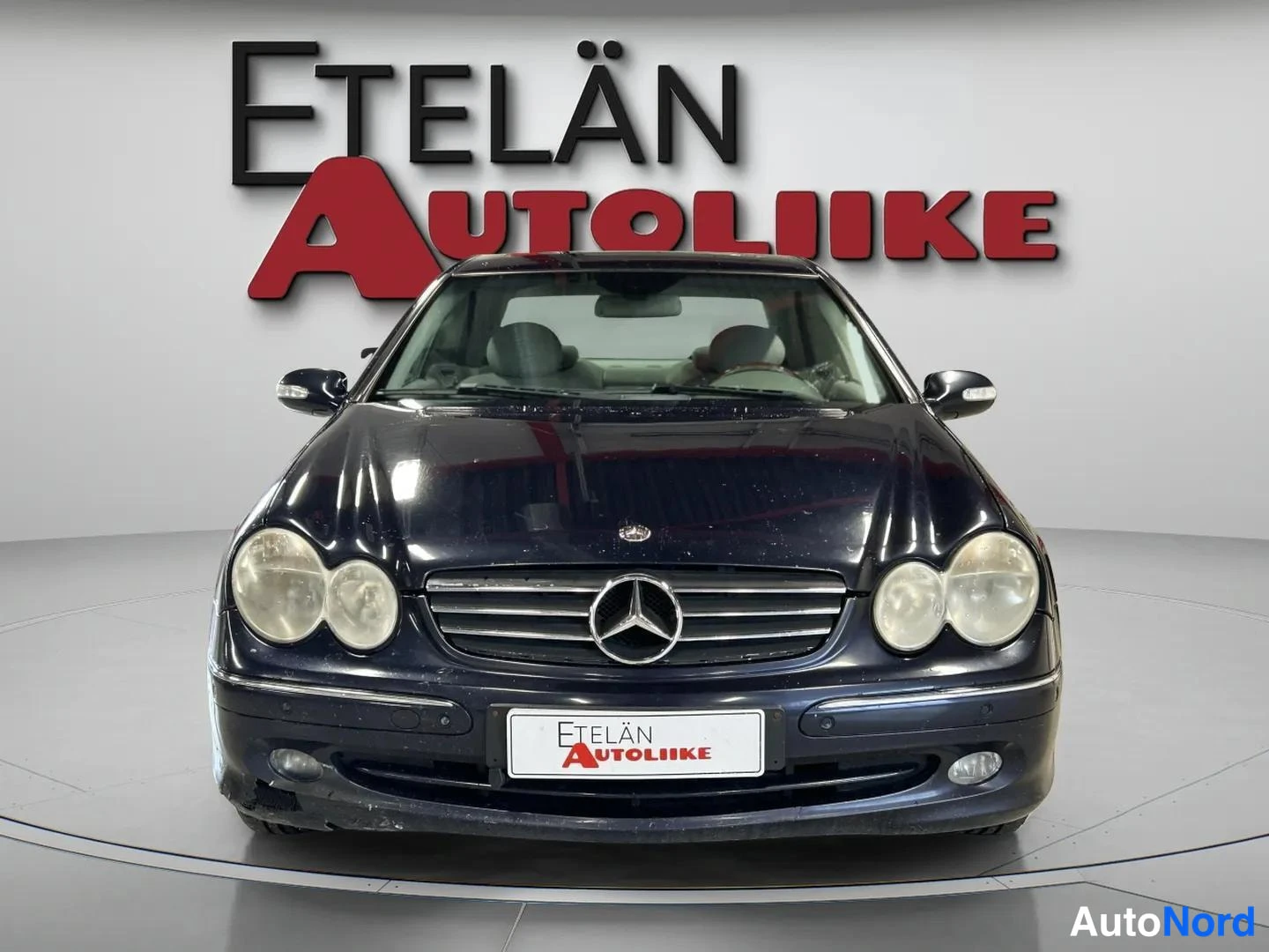 Edestä: Auto suoraan edestäpäin, tumma kylki ja etusäleikkö studiotaalustaa vasten.