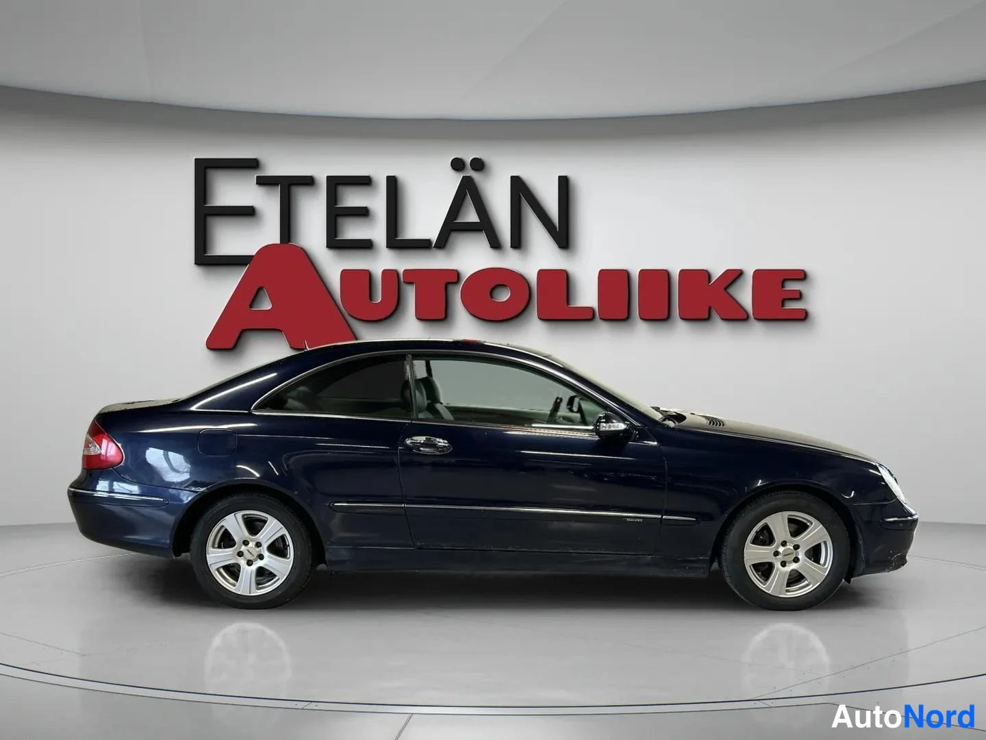 Etuviisto, nokka oikealle: Tummansininen coupe sivulta hieman keulaa kohden, keula oikealla, Etelän Autoliike-logo taustalla