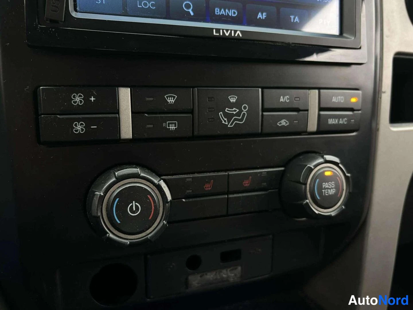 Muu: Lähikuva ilmastointipaneelista nappeineen (A/C, MAX A/C, AUTO) ja Livian merkityn radionäytön alareunasta.