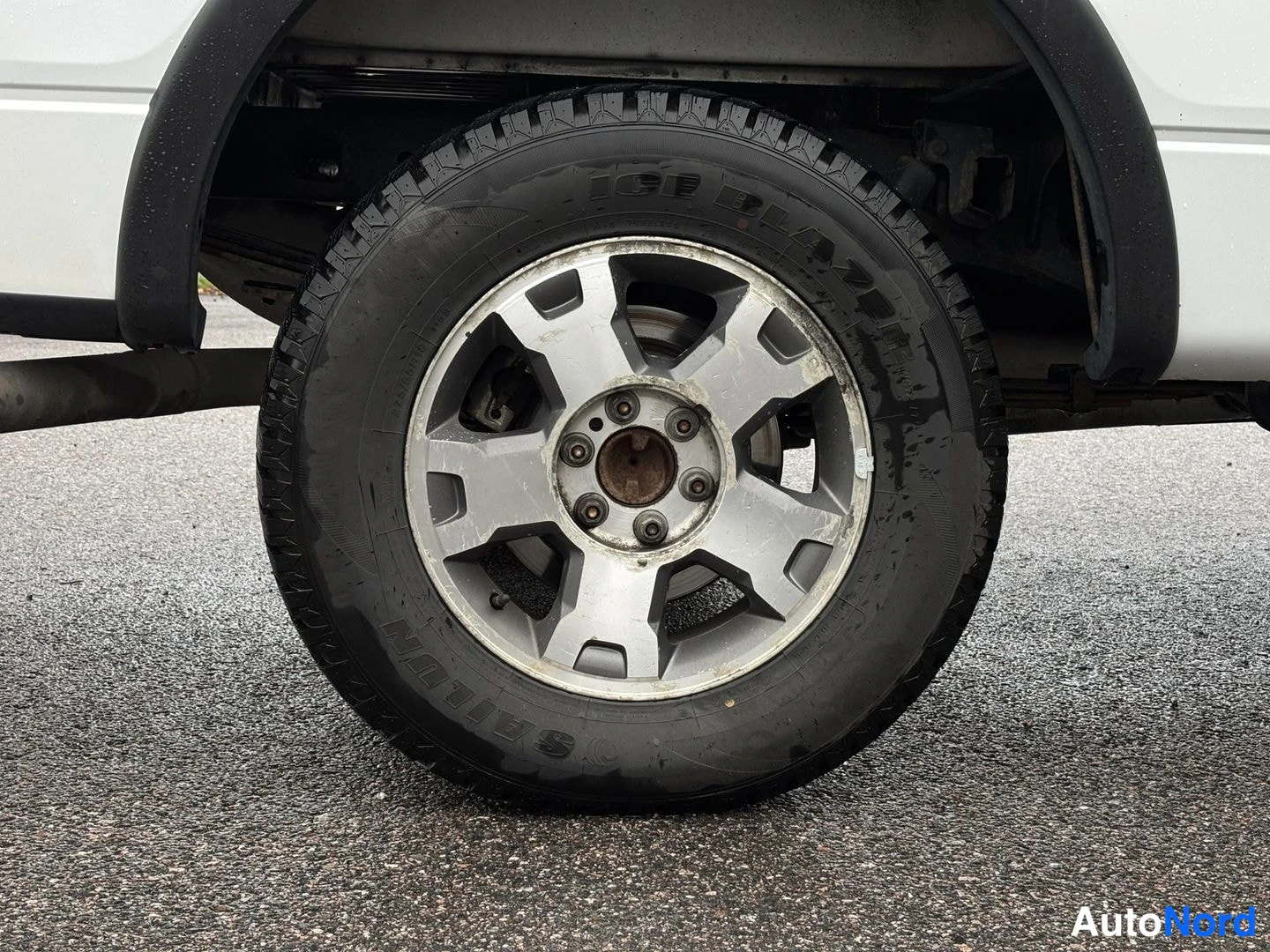 Muu: lähikuva auton pyörästä: hopea viisiteräinen vanne ja Sailun Ice Blade -rengassa, asvaltti mustan puoleista märkää.