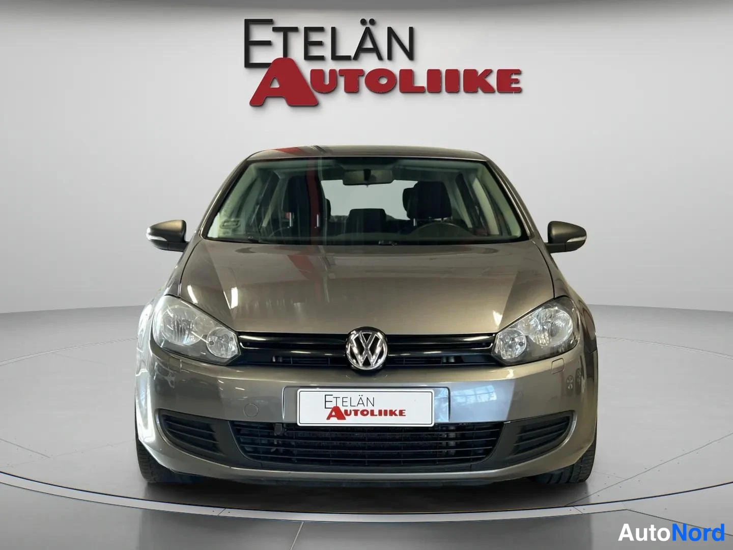 Edestä: Volkswagen Golf 2011, suora etunäkymä, harmaa etusäiliö ja VW-merkki näkyvät studiotaalustossa.