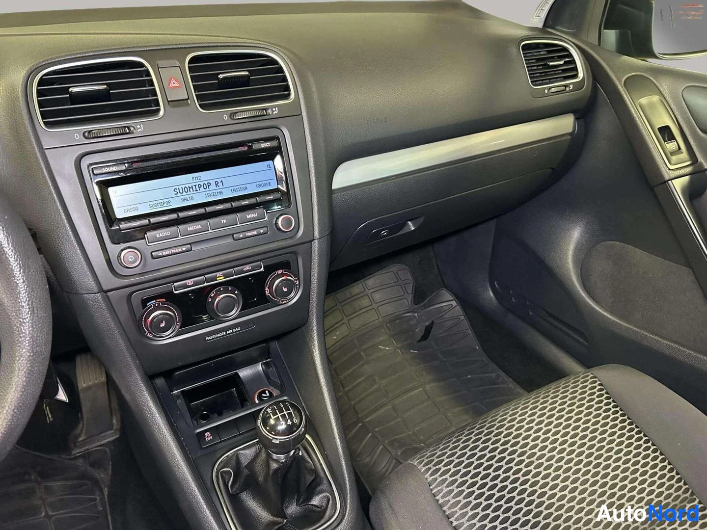 Muu: Keskiöconsole: Volkswagen-radio näytöllä 'SUOMIPOP R.1', manuaalivaihteiston vaihteenkytkin ja matkustajan matto