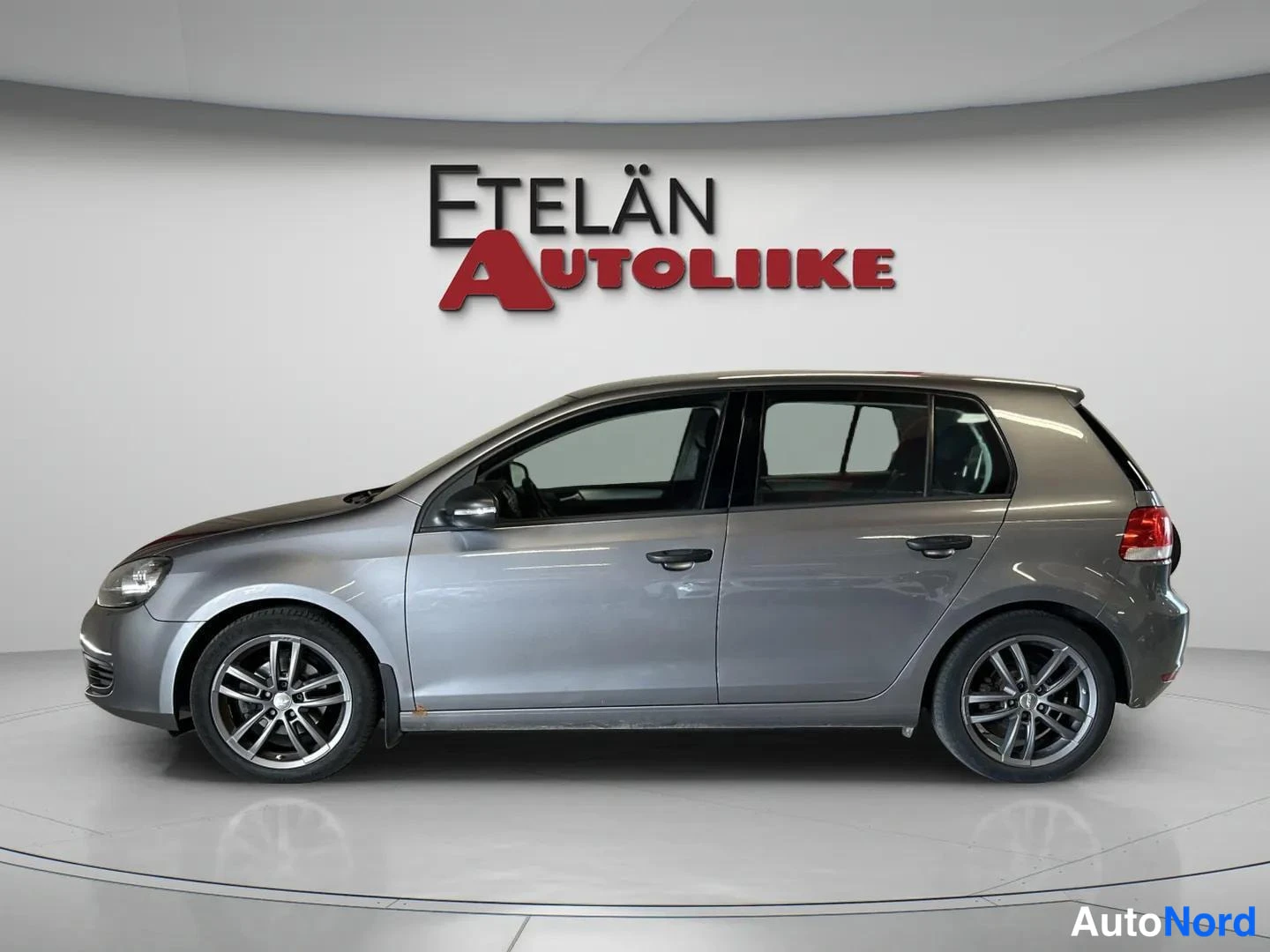 Sivulta: Volkswagen Golf 2011, sivunäkymä vasemmalta, harmaa 5-ovinen viistoperä kevytmetallivanteilla studiotaalustossa.