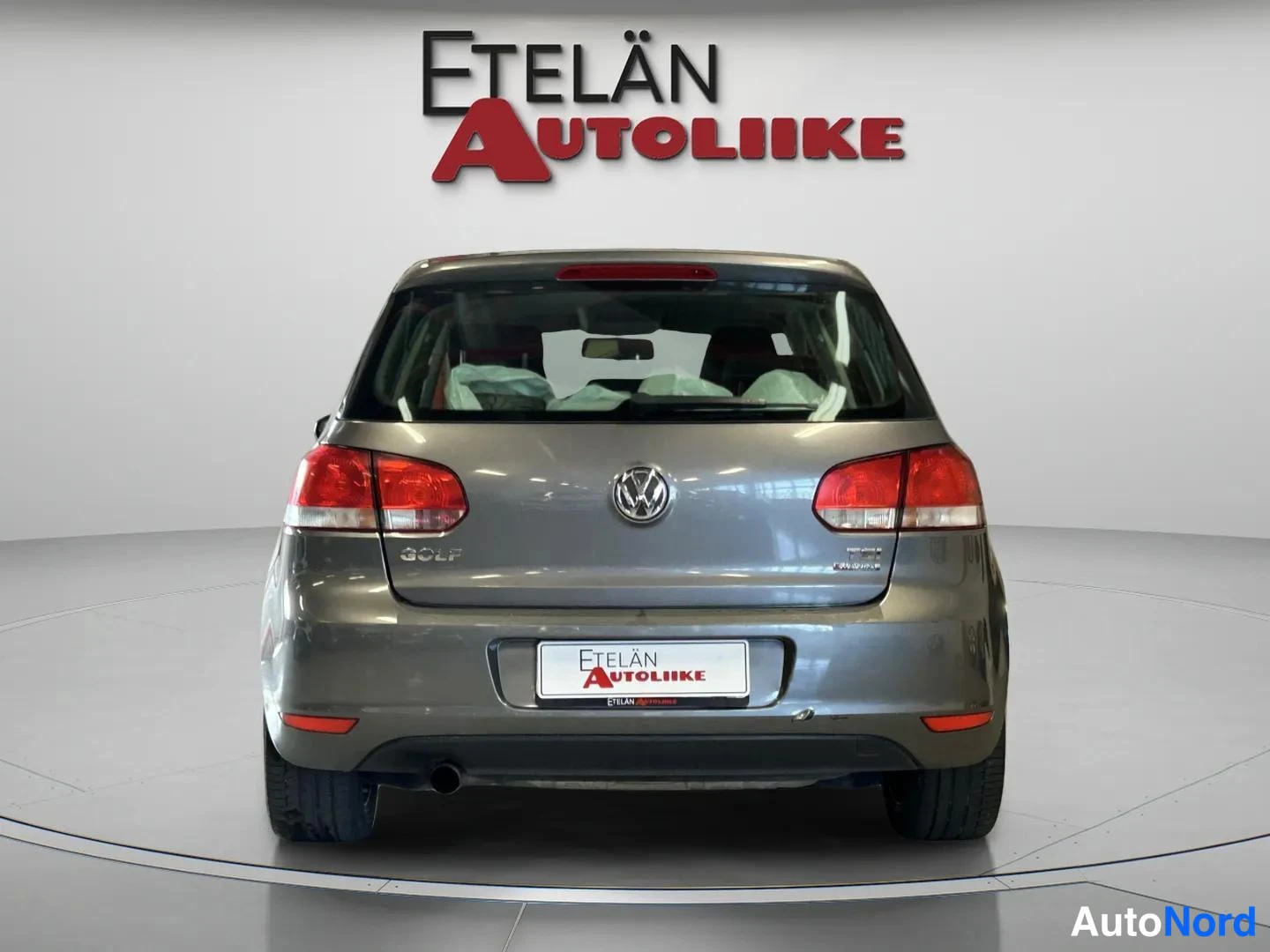 Takaa: Harmaan viistoperäisen auton takaosan suora etunäkymä: punaiset takavalot, VW-merkki ja GOLF-teksti takaluukussa.