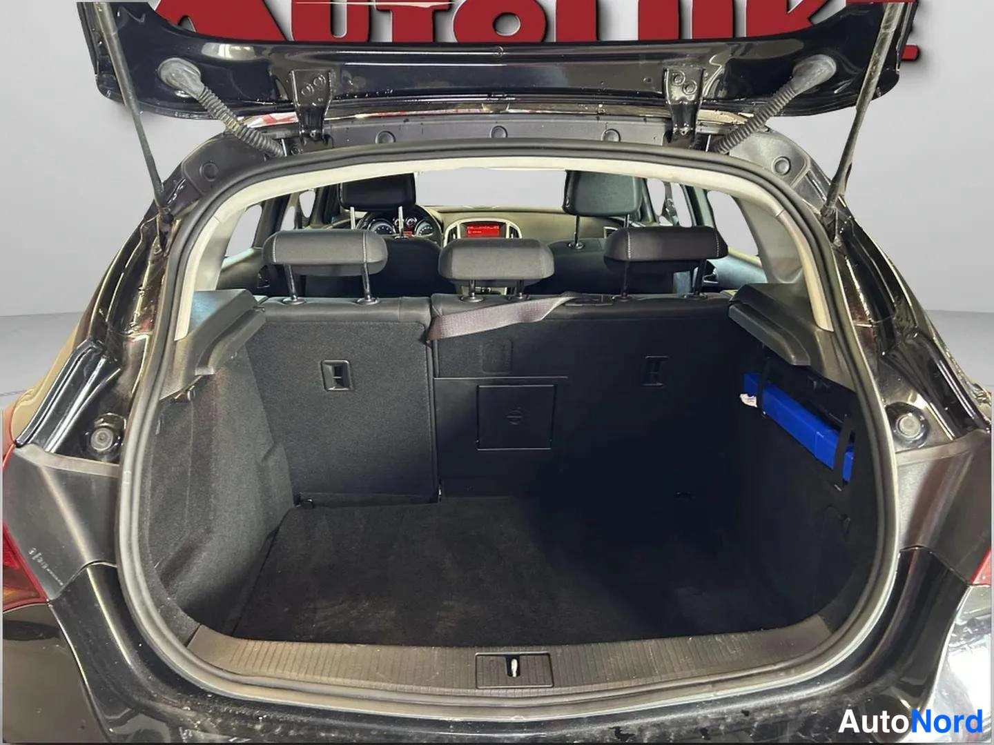 Takaa: View of a dark-colored station wagon trunk with the tailgate open. Three rear seat headrests are visible behind the cargo area. A blue rectangular object sits i